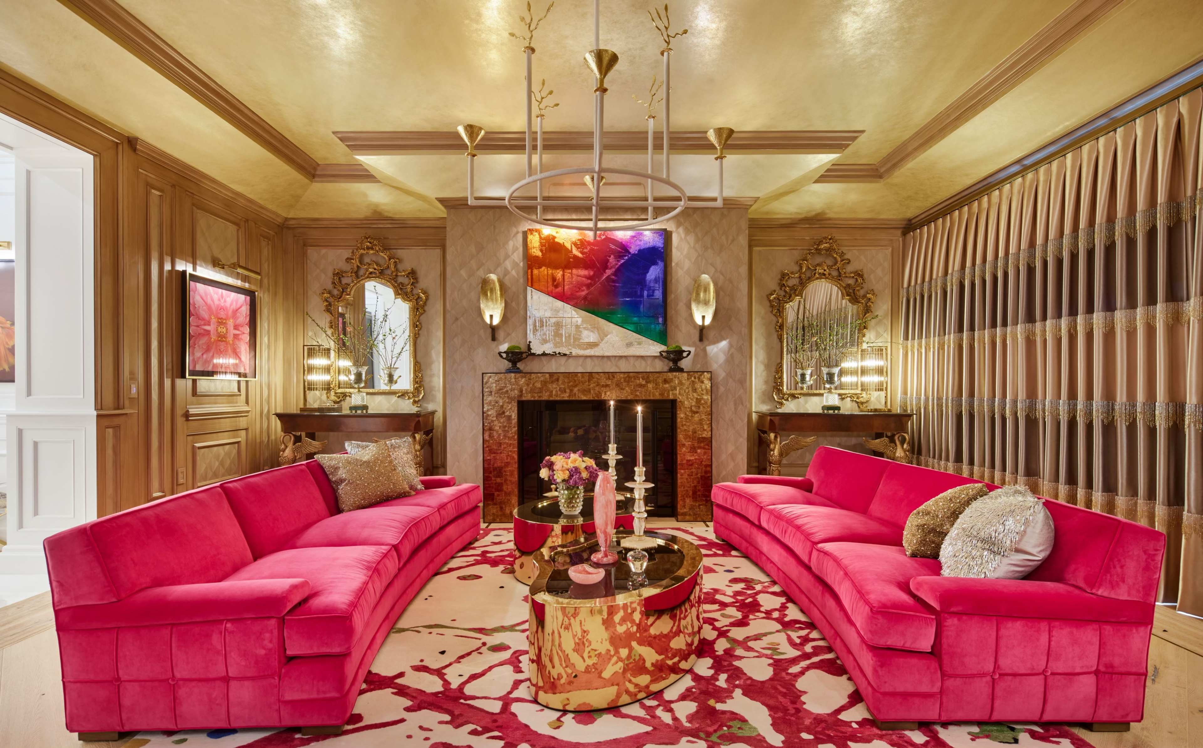 A luxurious living room features two pink sofas facing each other, a circular coffee table, a fireplace, and decorative mirrors against a gold-hued wall.