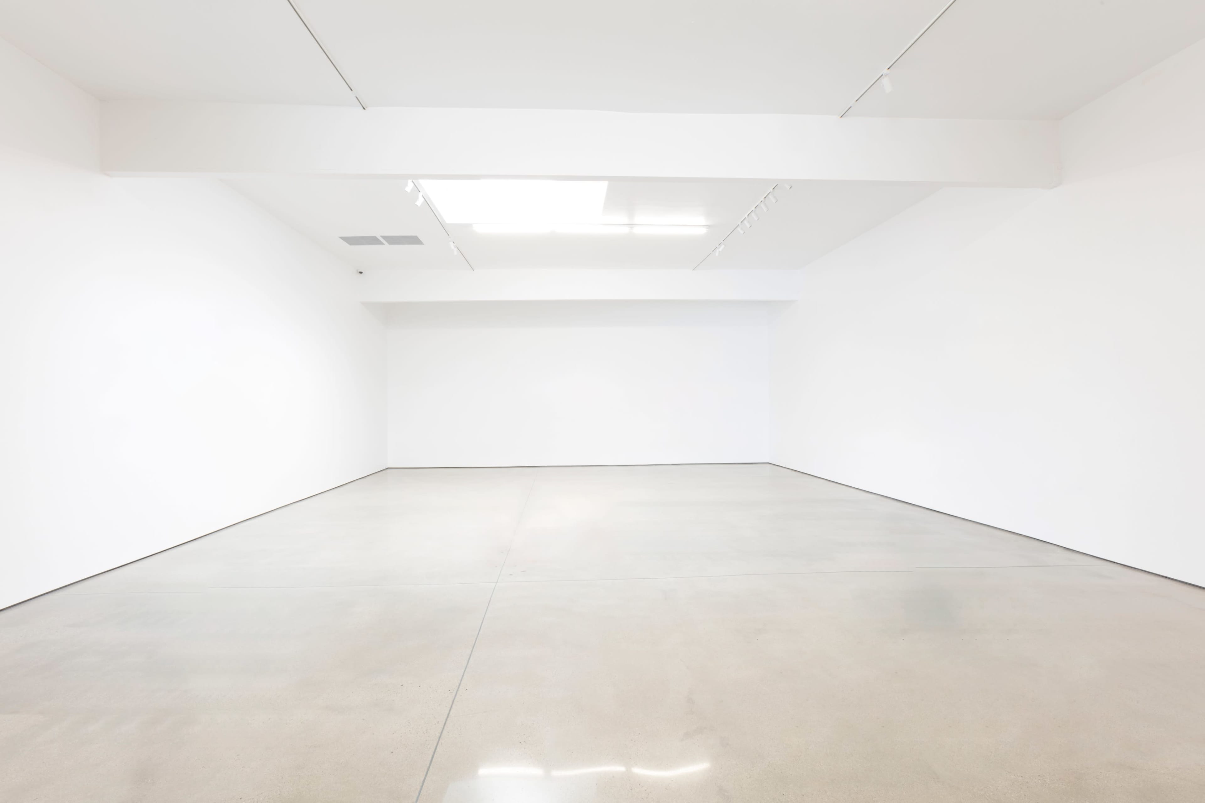 A spacious, empty gallery with white walls and a polished concrete floor.