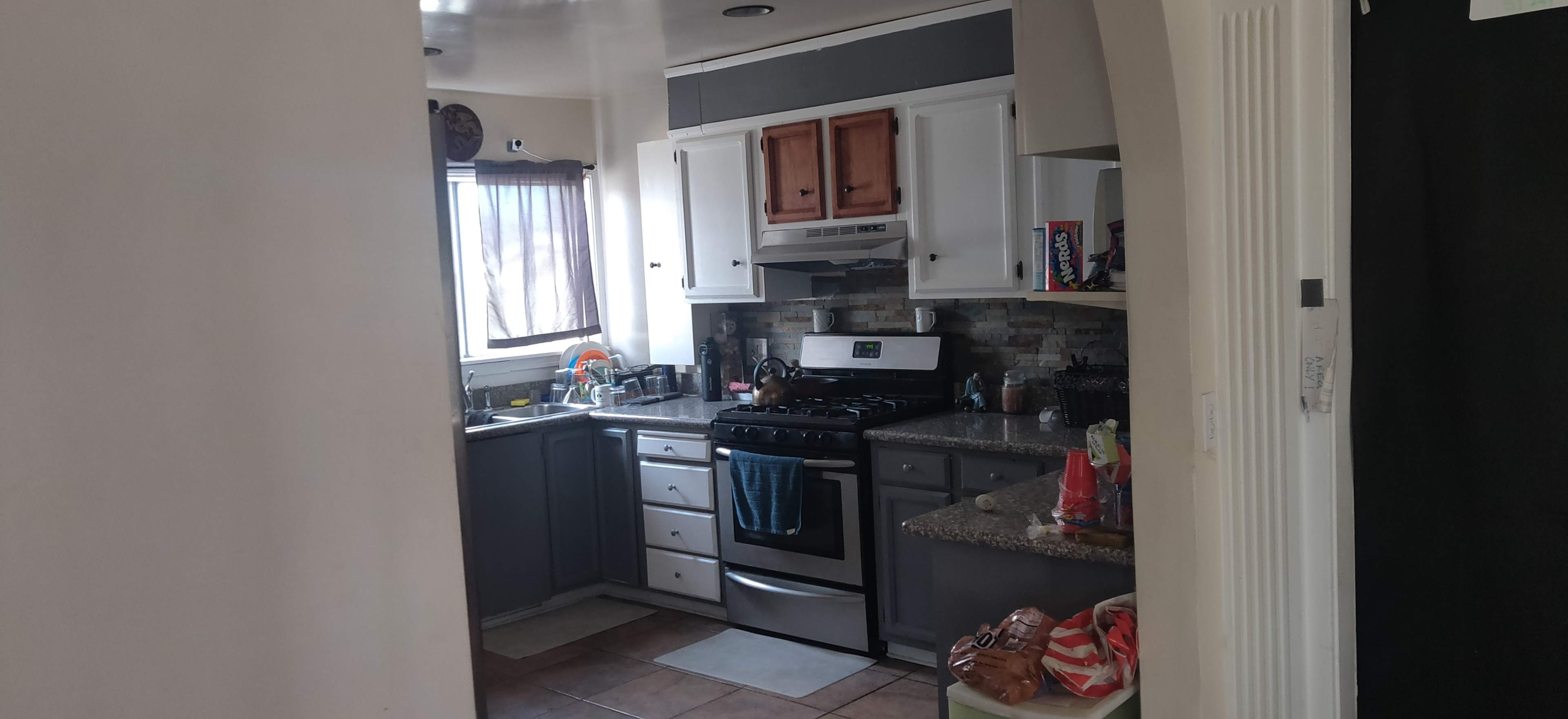 The image shows a kitchen with gray and white cabinetry, a stainless steel stove, and a countertop with various kitchen items.