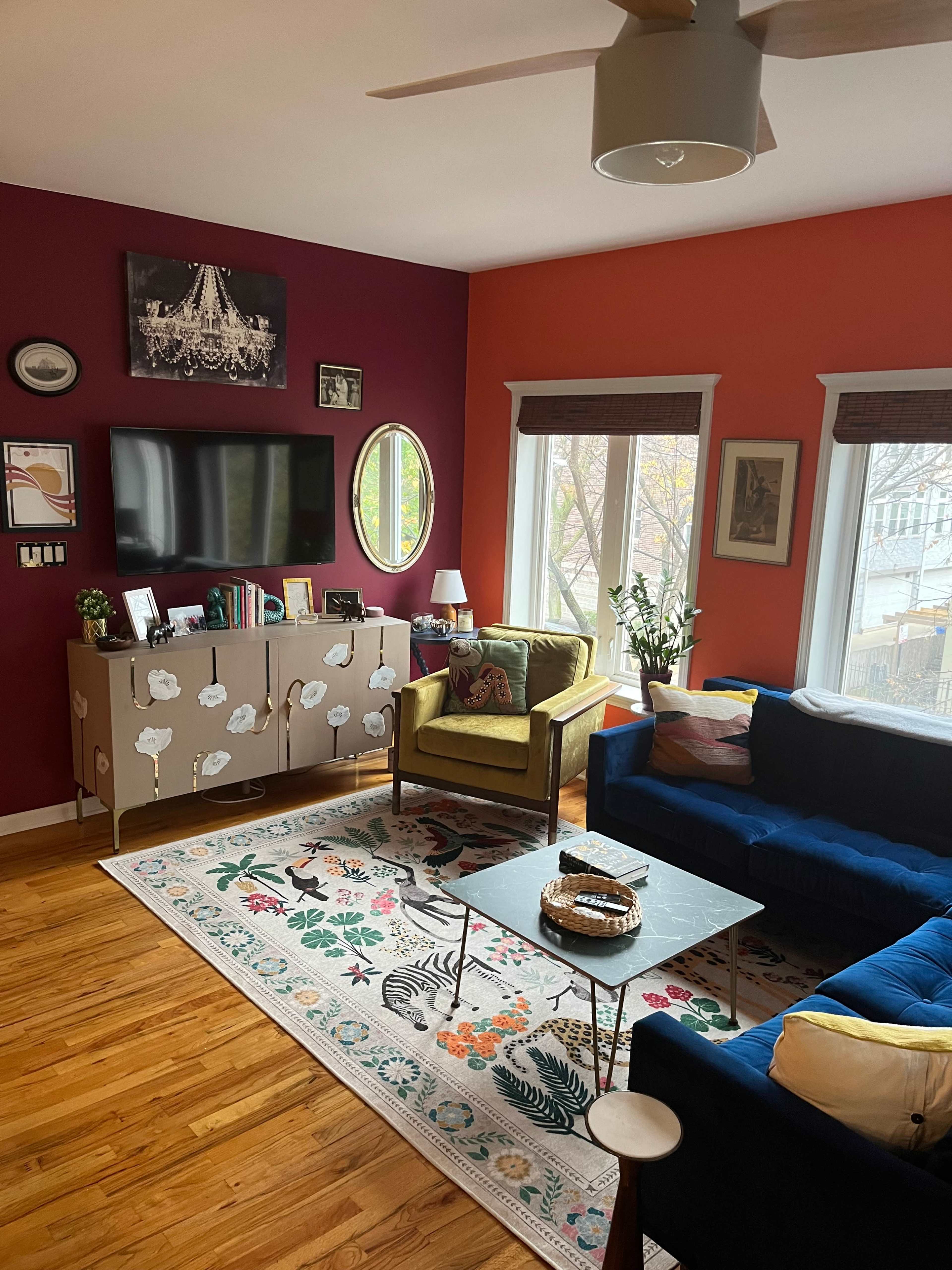 A living room with colorful walls, a television mounted above a cabinet, a blue couch, a yellow armchair, and a decorative rug on a wooden floor.