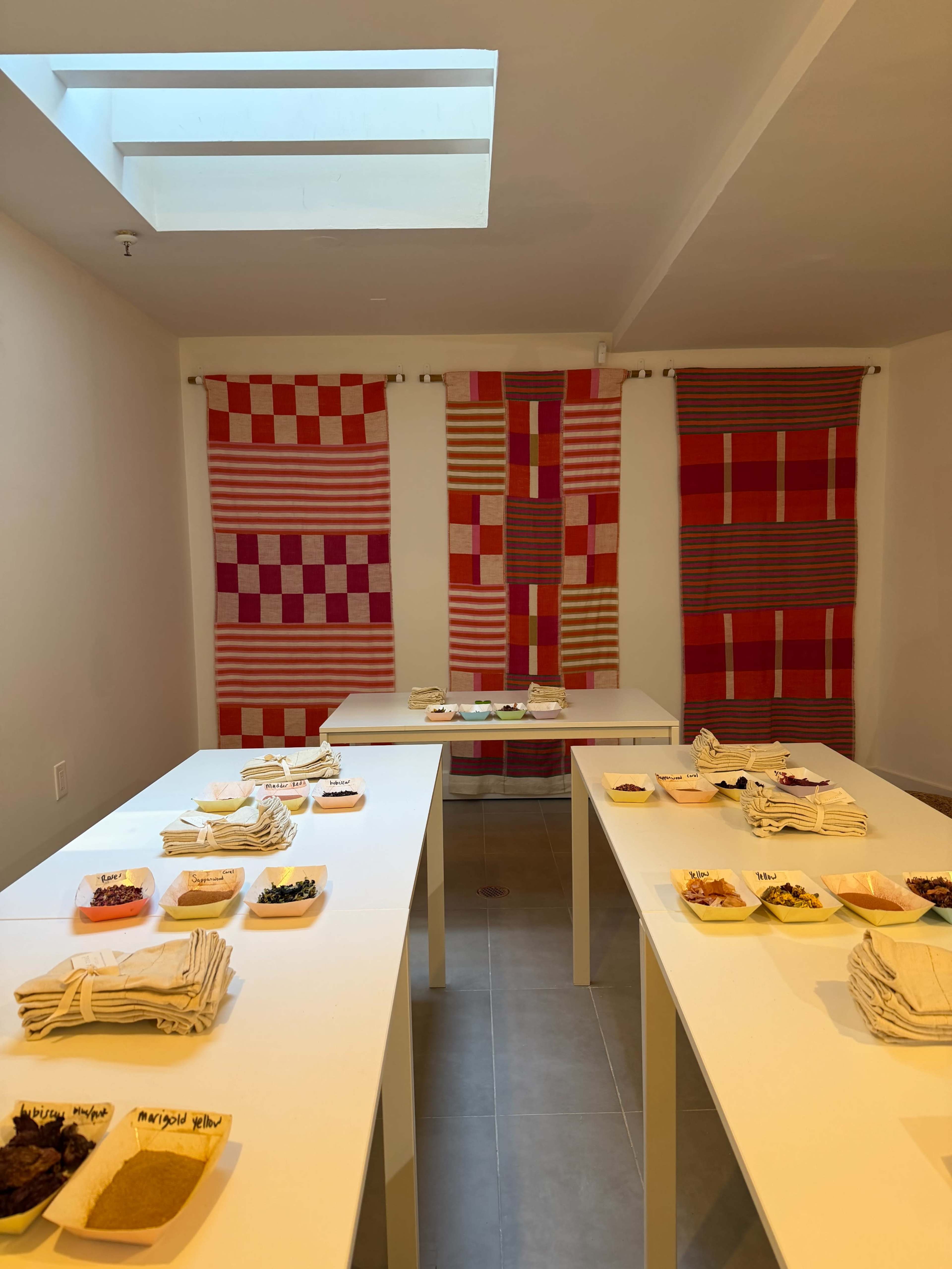 The room features white tables arranged with various dishes and ingredients, flanked by colorful woven textiles hanging on the walls.