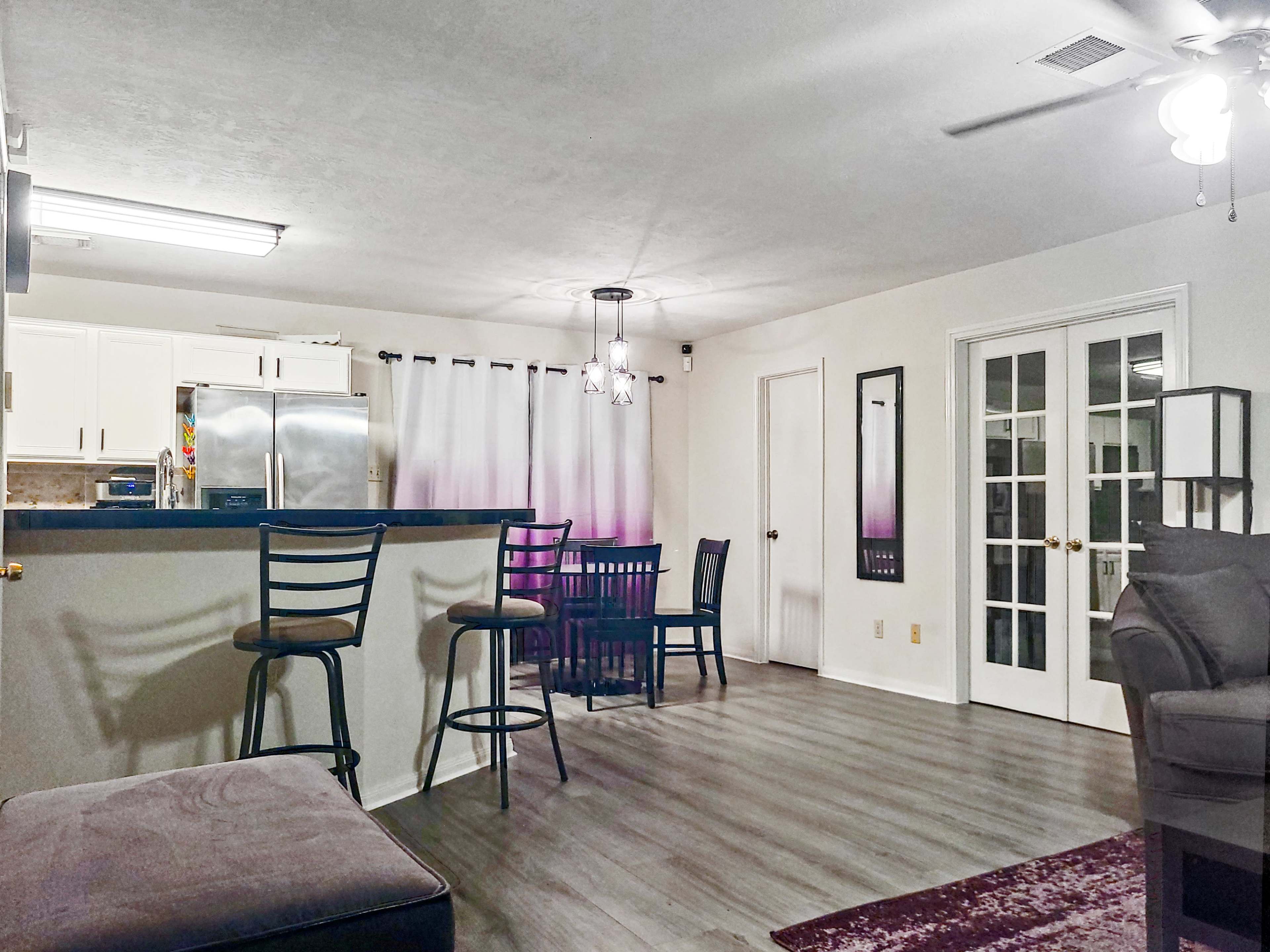 A modern living space with a kitchen area featuring bar stools, a dining table, and French doors leading to another room.