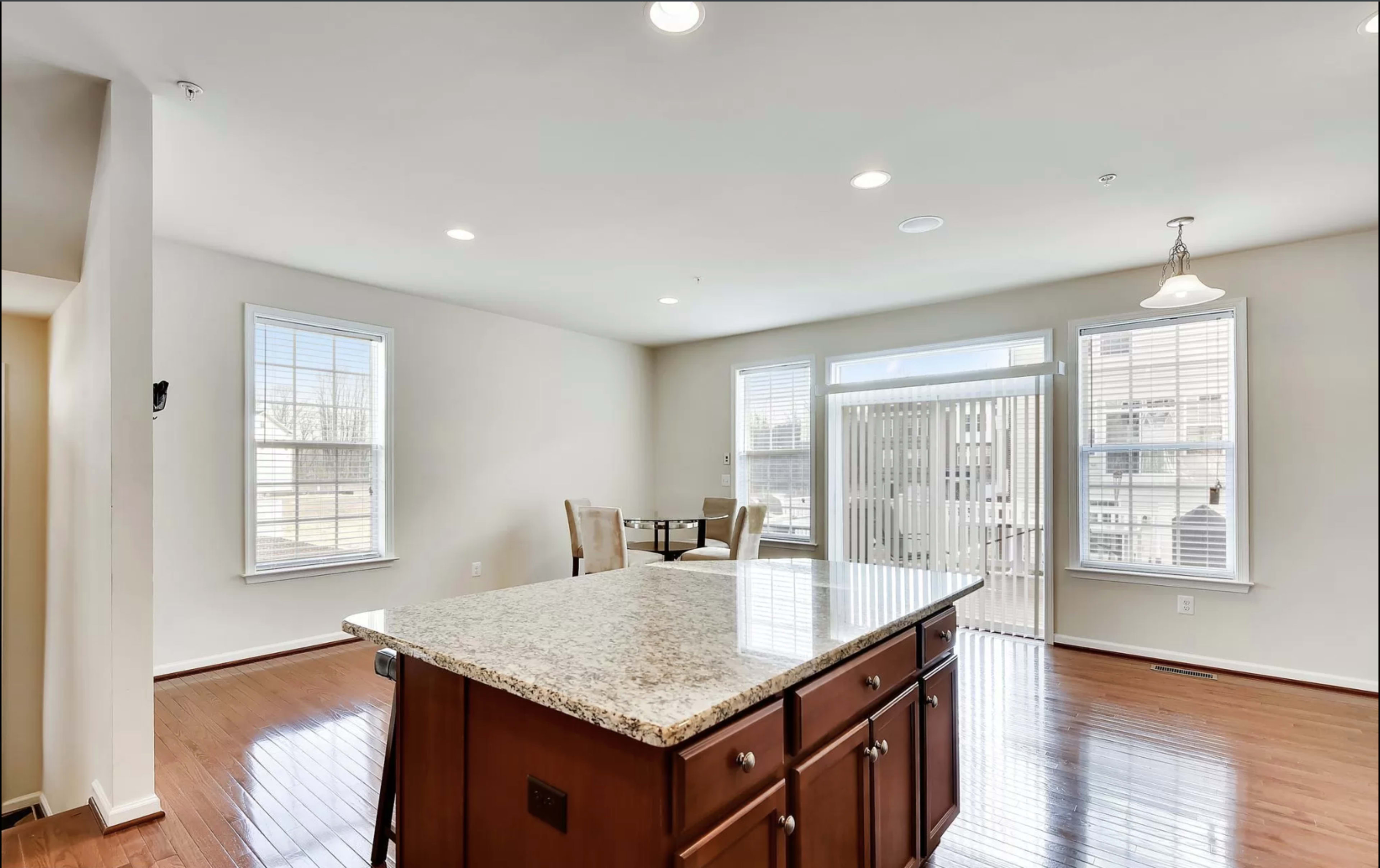 A spacious kitchen area features a granite island with wooden cabinetry, illuminated by recessed lighting and natural light from large windows.