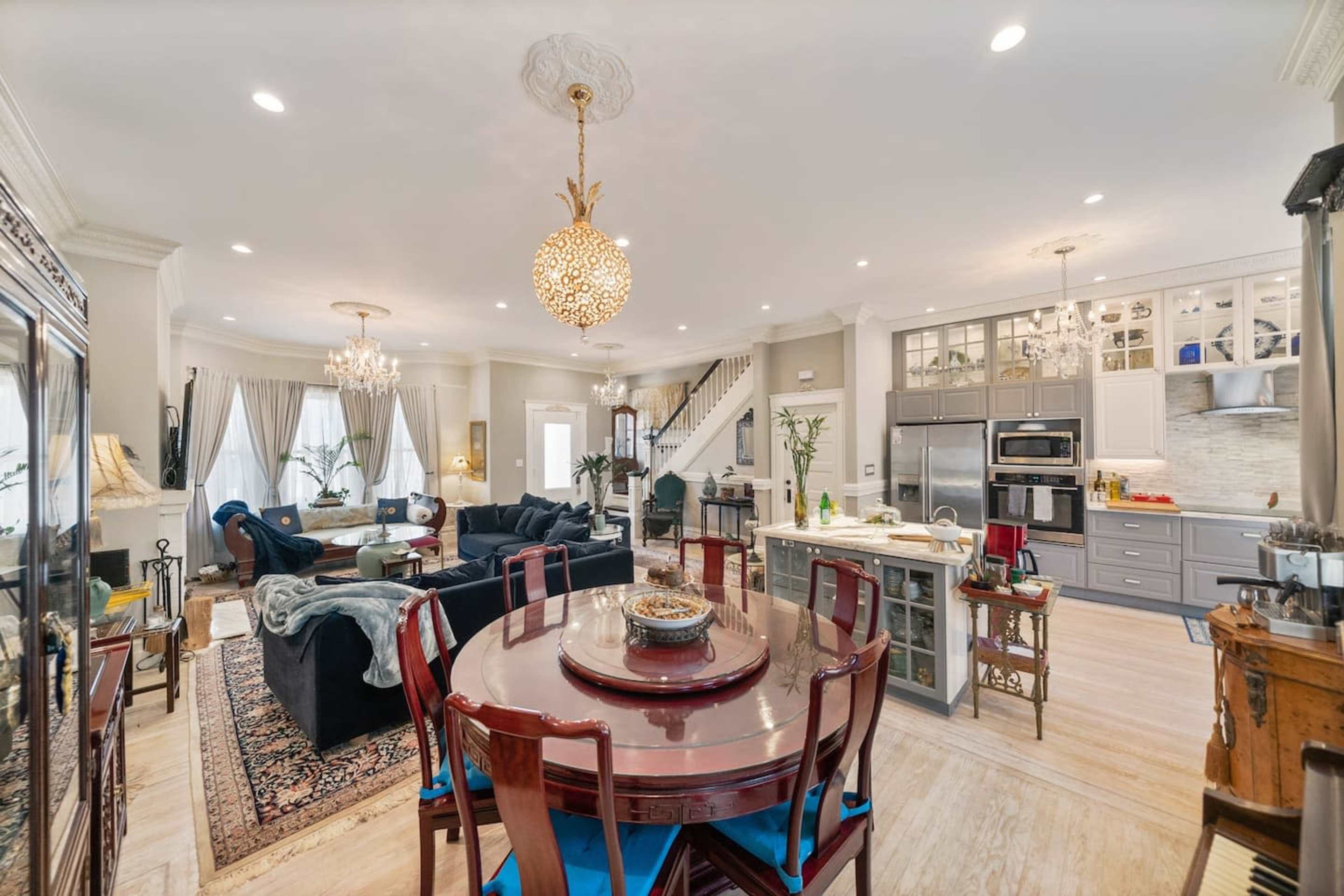 A spacious, open-concept living and dining area featuring a round dining table, a modern kitchen with stainless steel appliances, and a cozy seating area with dark sofas.