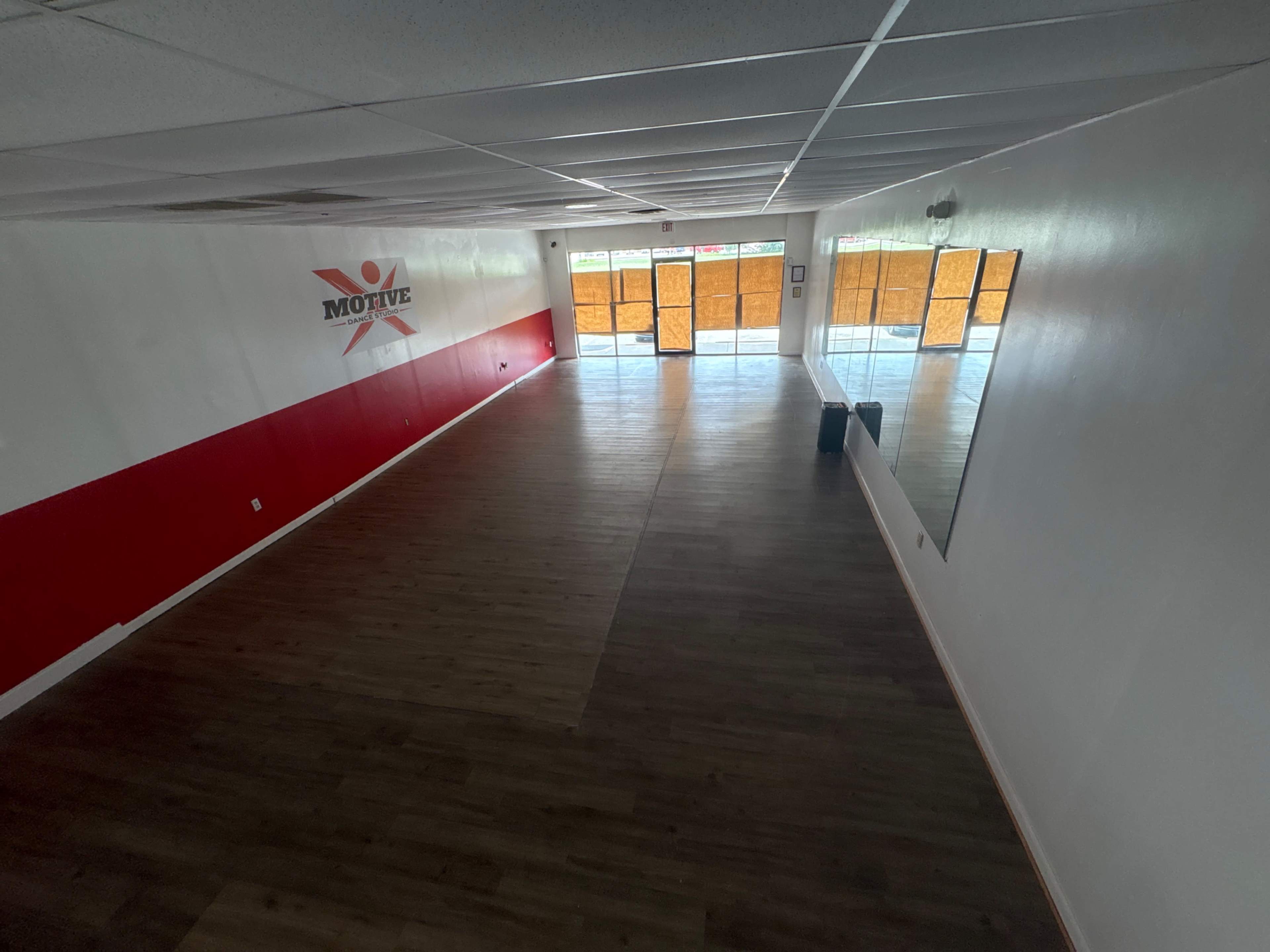 The image shows an empty fitness studio with a red and white wall labeled "MOTIVE" and large windows covered with orange material.