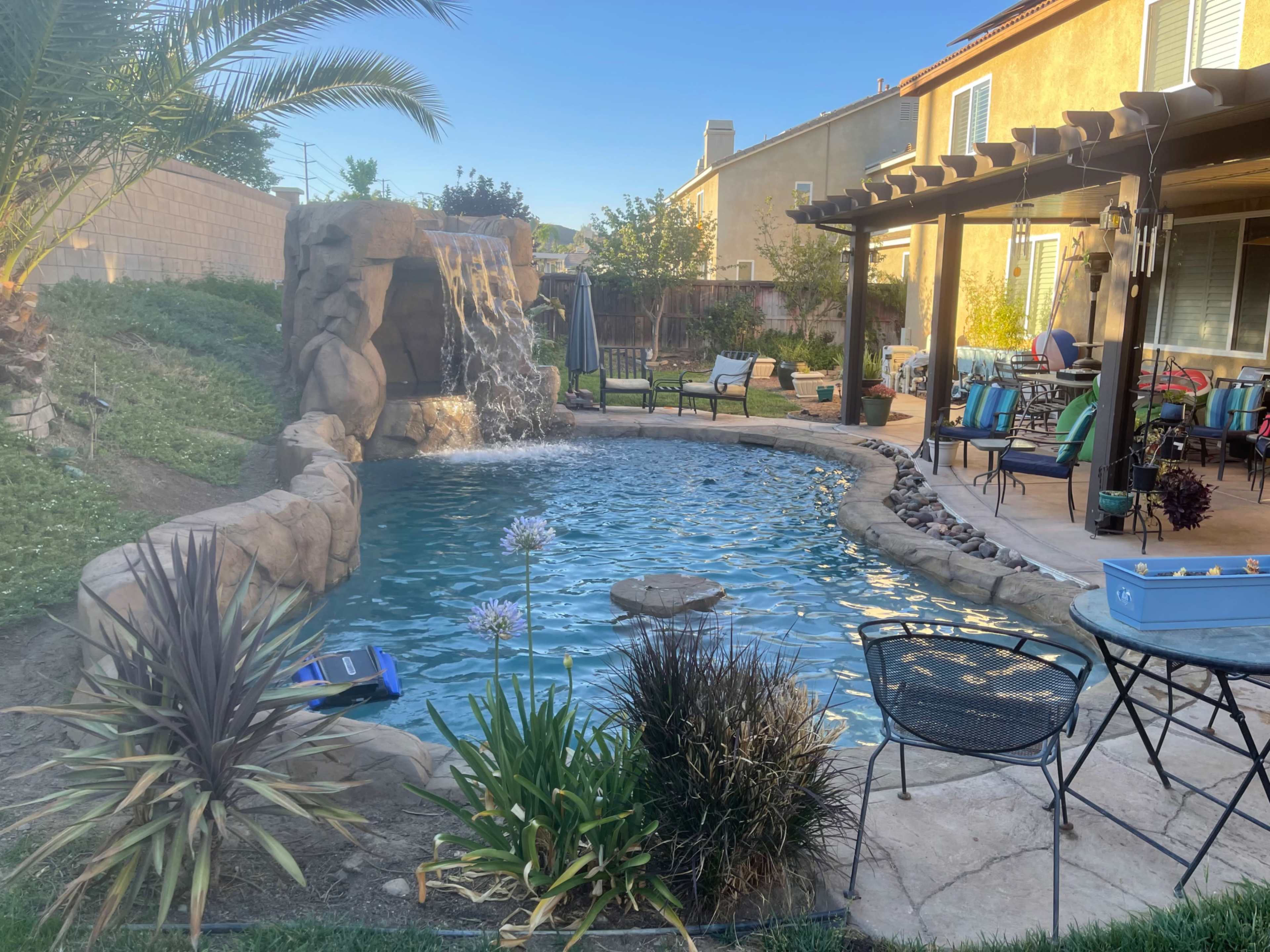 A backyard swimming pool with a rock waterfall, surrounded by lounge chairs and a patio area.
