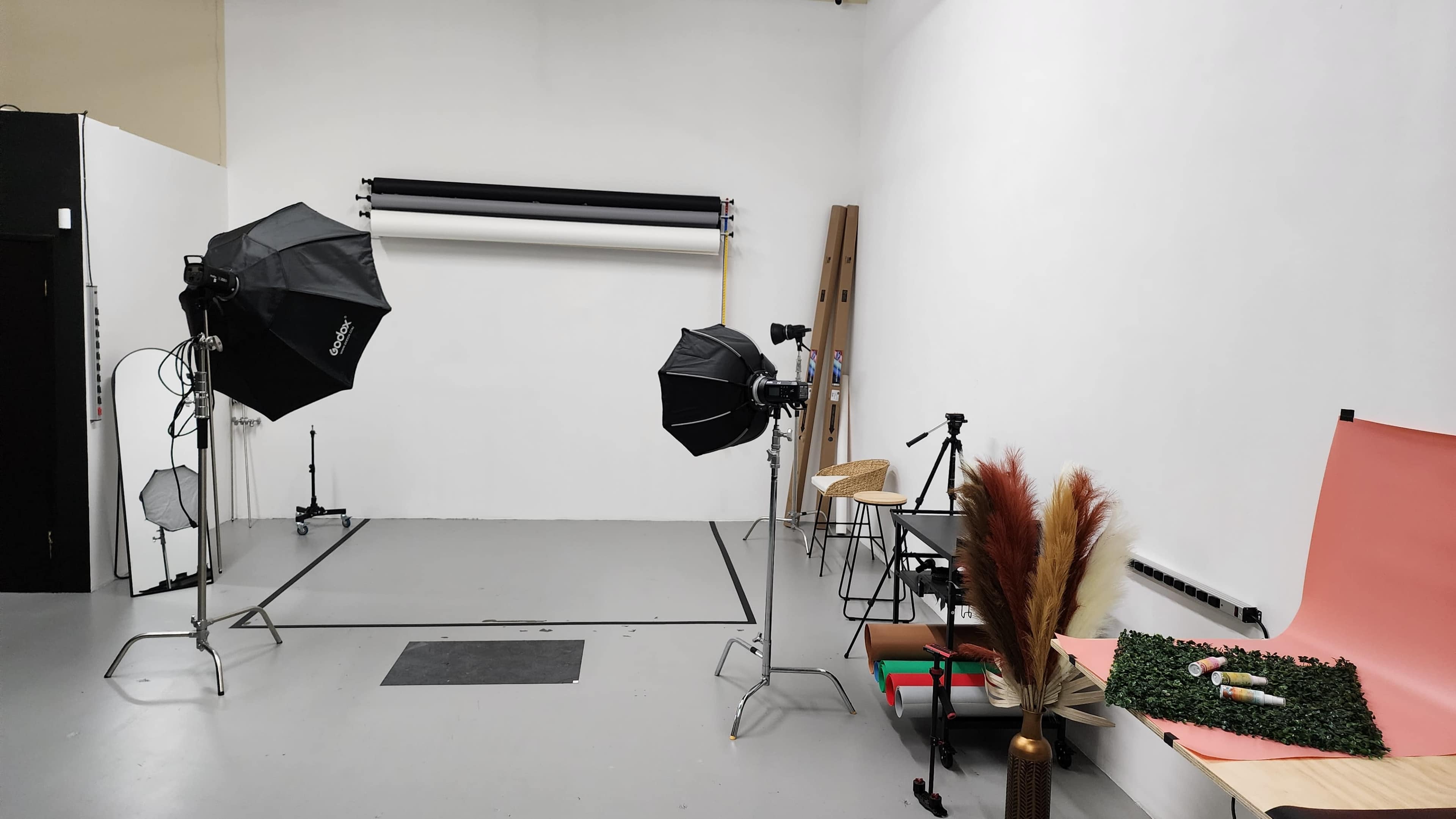 A photography studio features various equipment, including lights, backdrops, and props arranged in a spacious area.