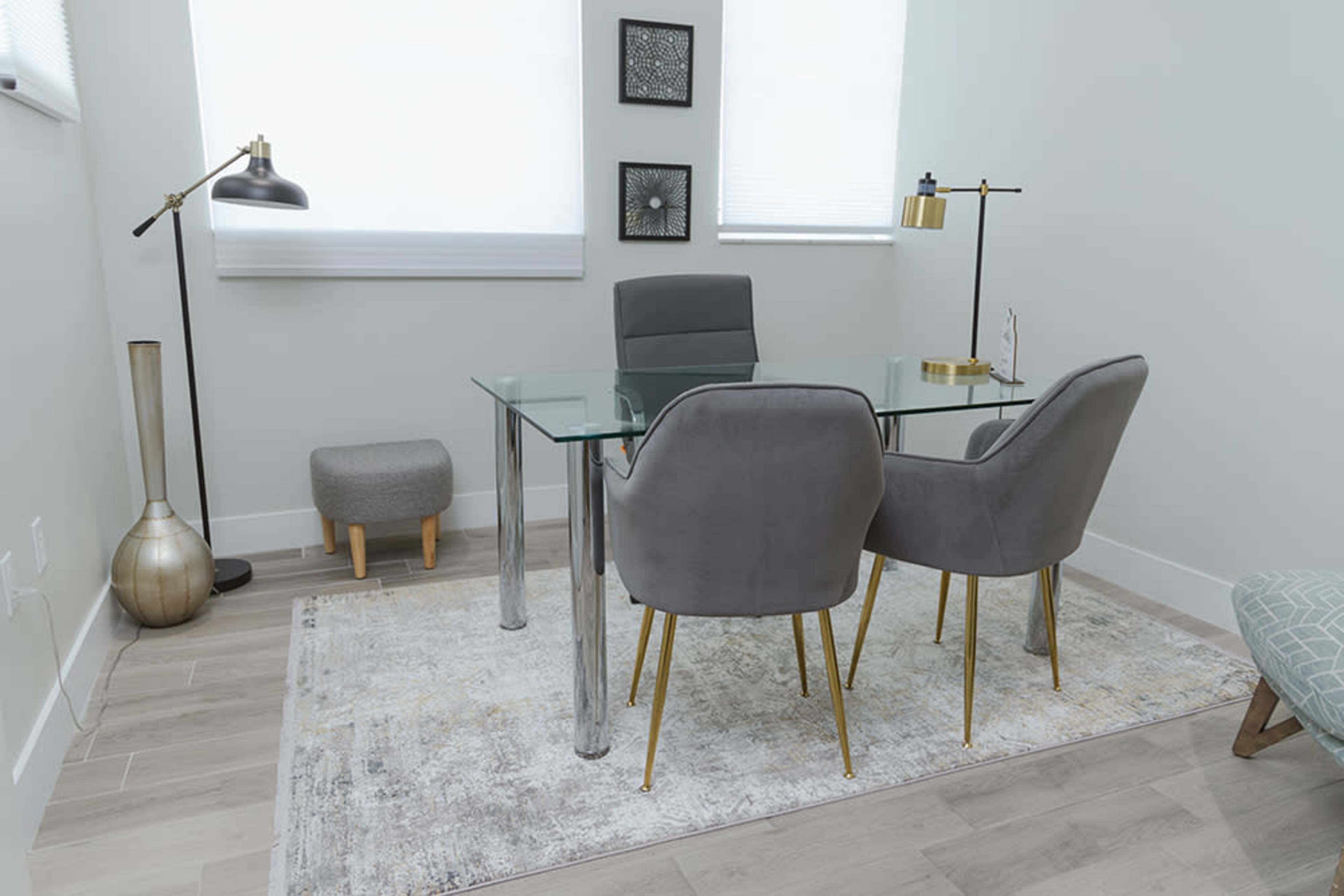 A modern office space featuring a glass desk with two gray chairs, a lamp, and a rug on a wooden floor.