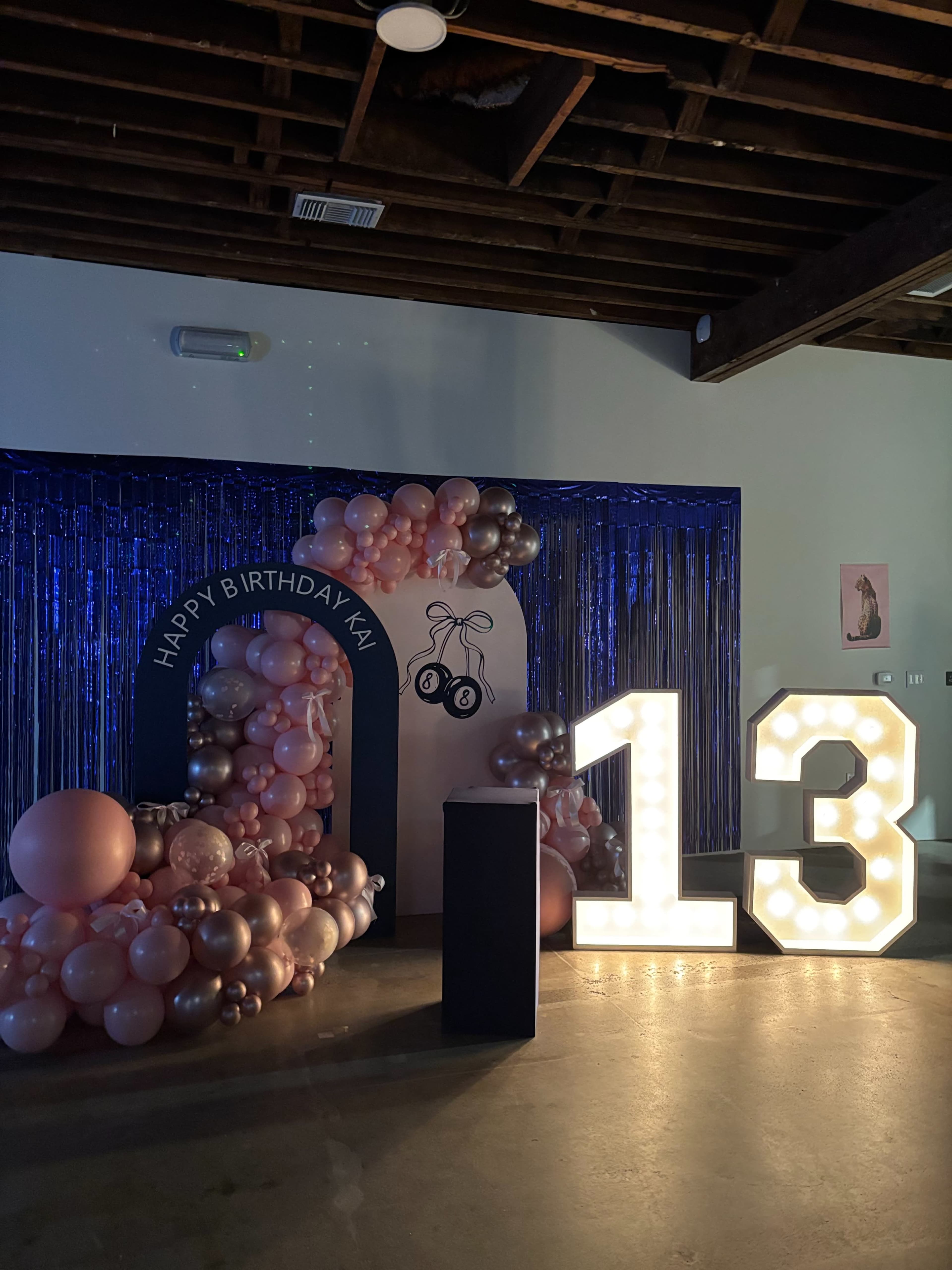 The image features a decorated birthday area with large illuminated numbers "13," a balloon arch, and a banner that reads "HAPPY BIRTHDAY KAI."