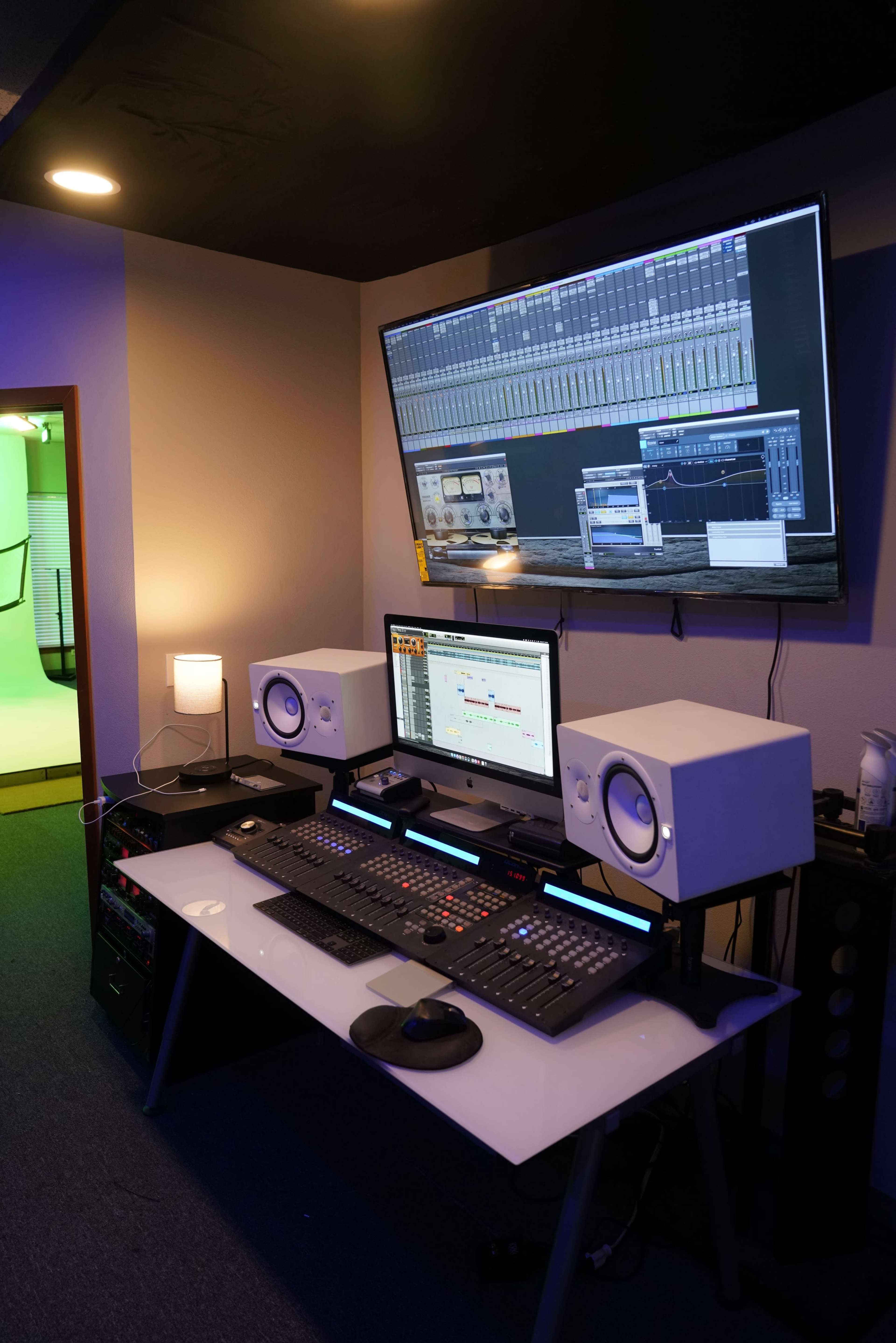A modern music production studio featuring a central desk with audio equipment, two monitors, and studio speakers.