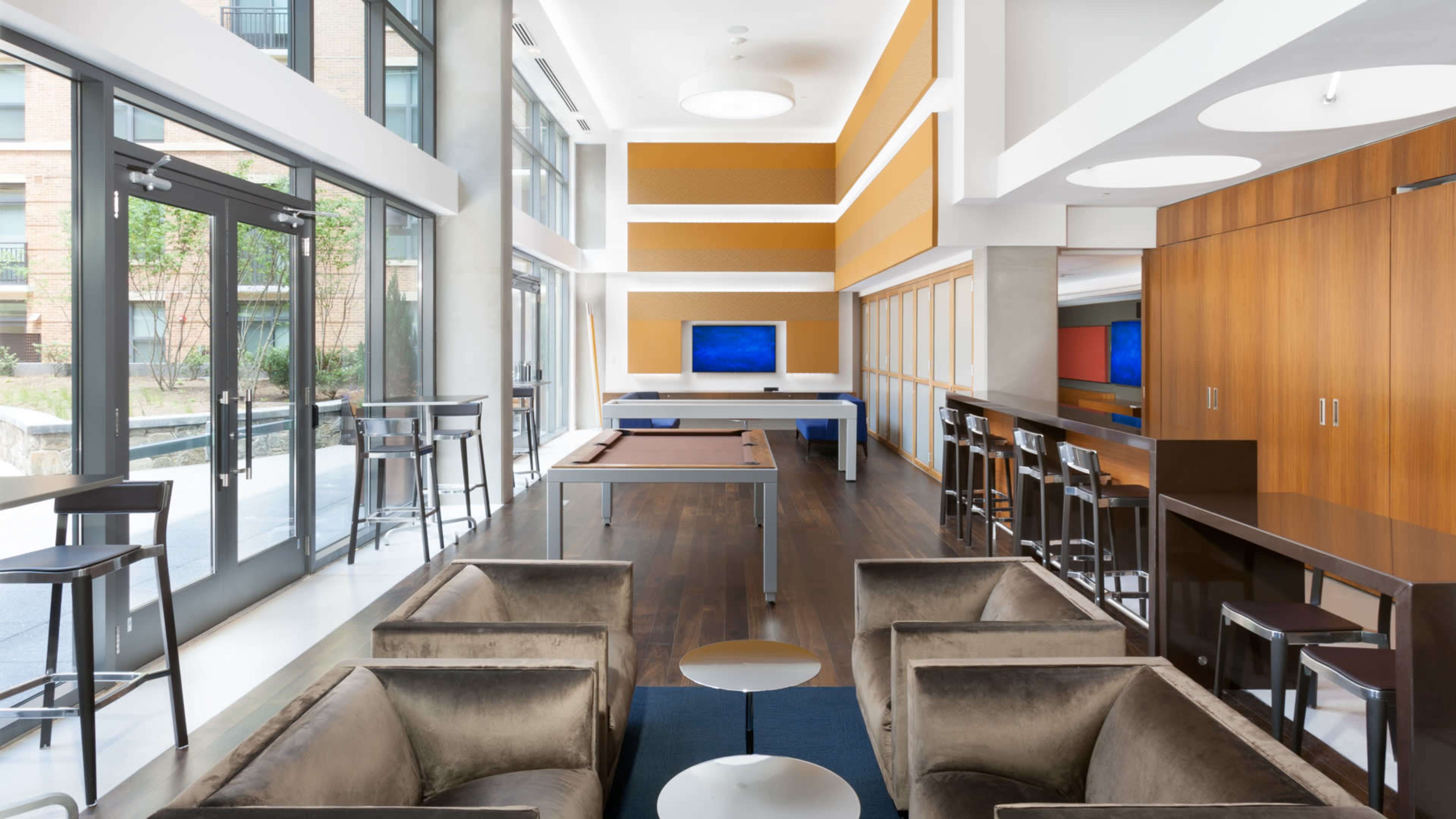 A modern lounge area featuring sofas, a pool table, and large windows that allow natural light to enter.