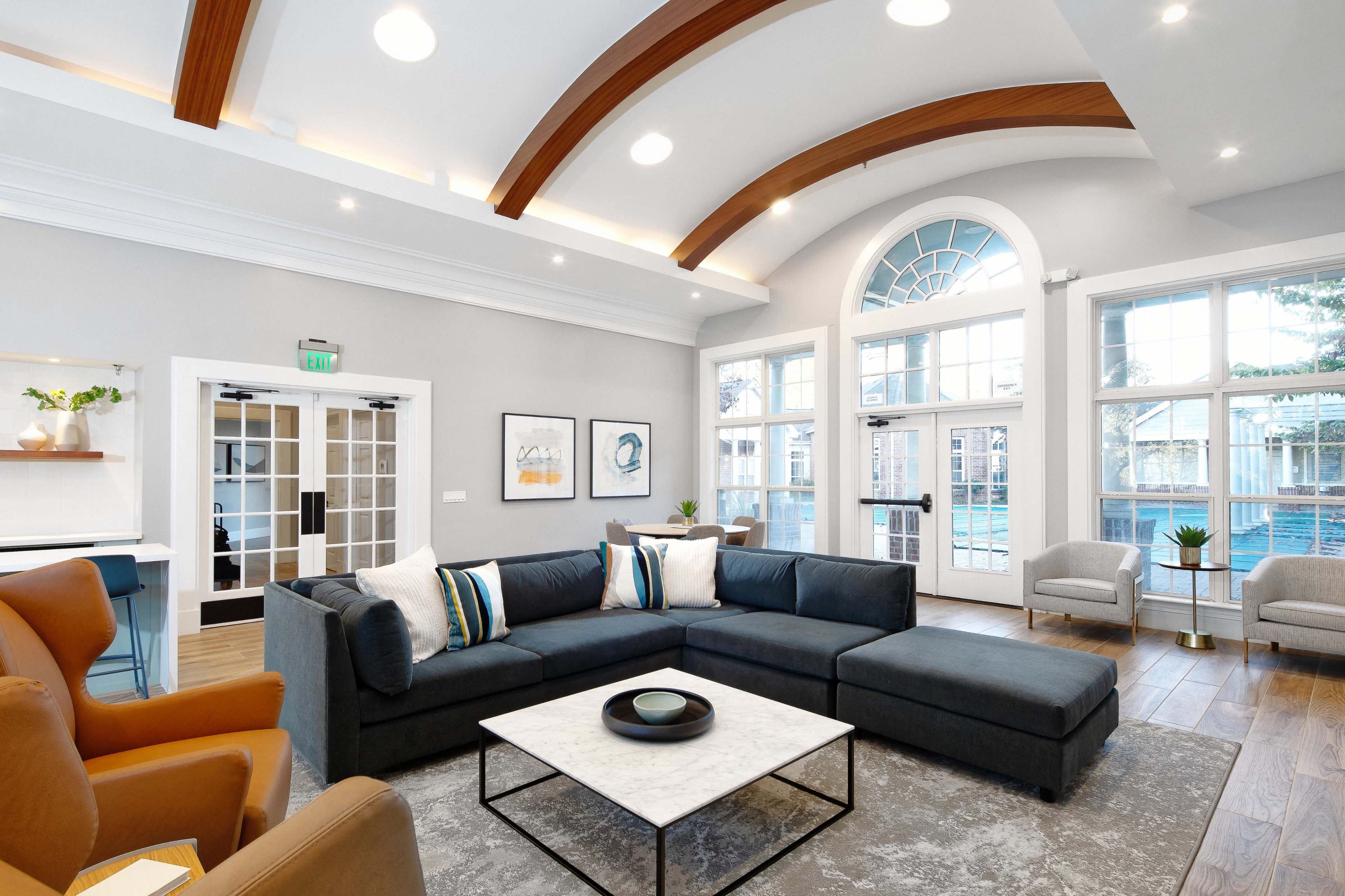 The image shows a modern living area with a sectional sofa, a marble coffee table, and large windows allowing natural light to enter the space.