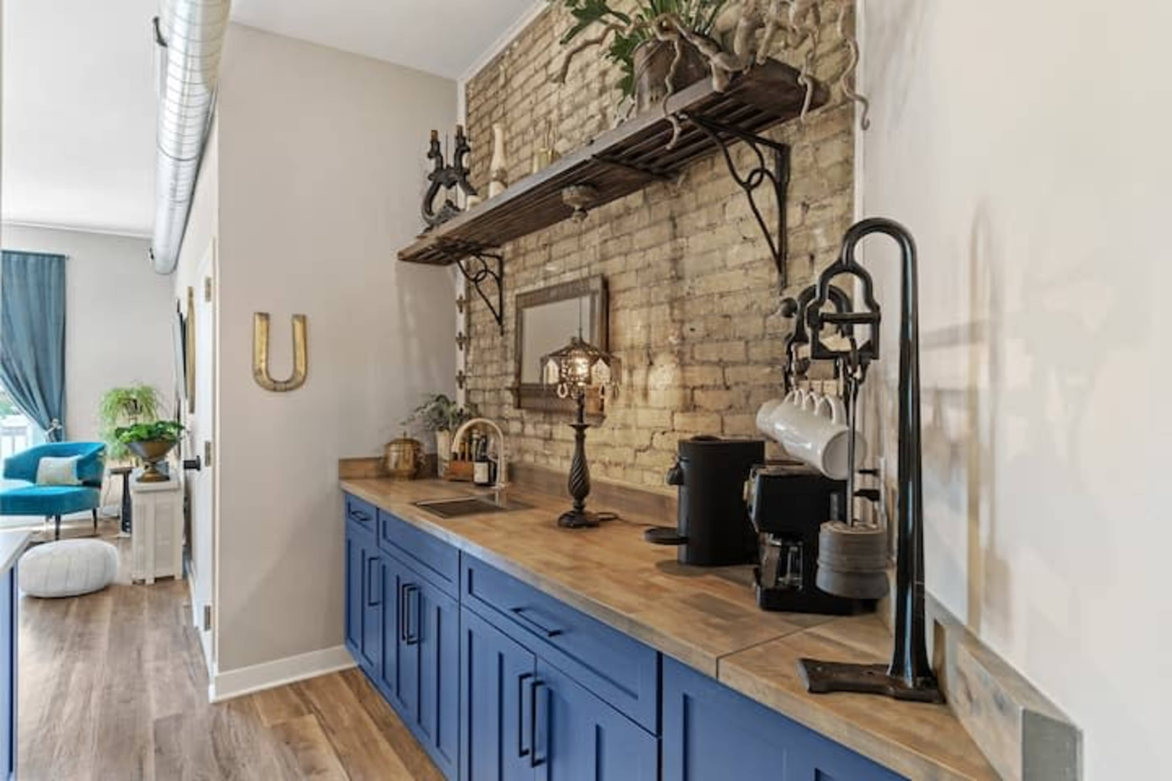 A kitchen area featuring blue cabinets, a wooden countertop, and a brick wall with decorative shelves.