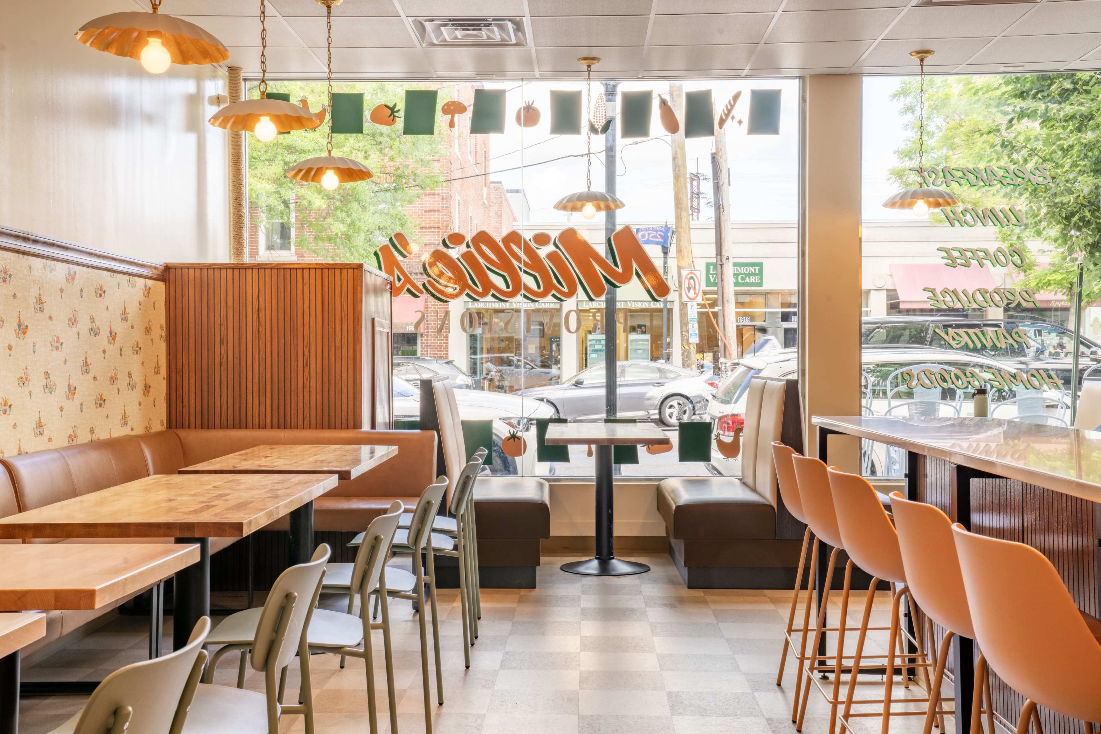 The image shows a bright and modern cafe interior with seating areas, large windows, and decorative light fixtures.