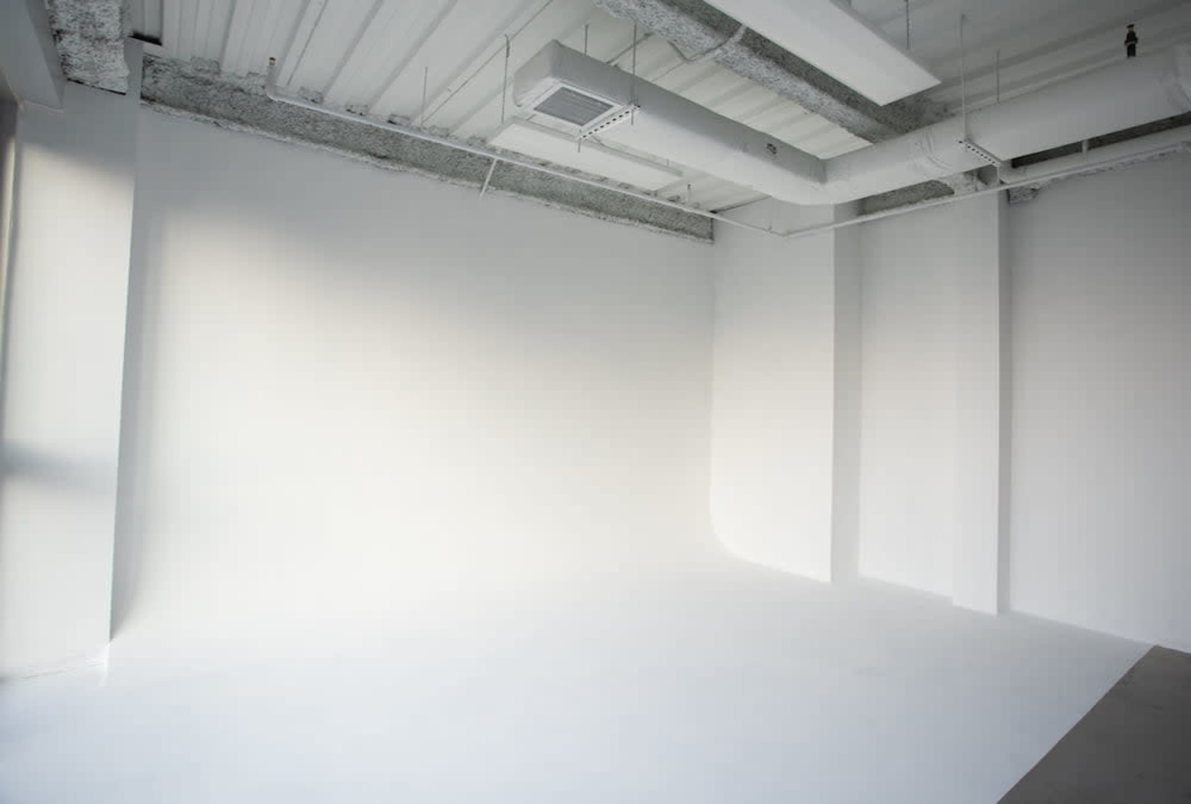 A large, empty room with white walls and a smooth white floor, illuminated by natural light.