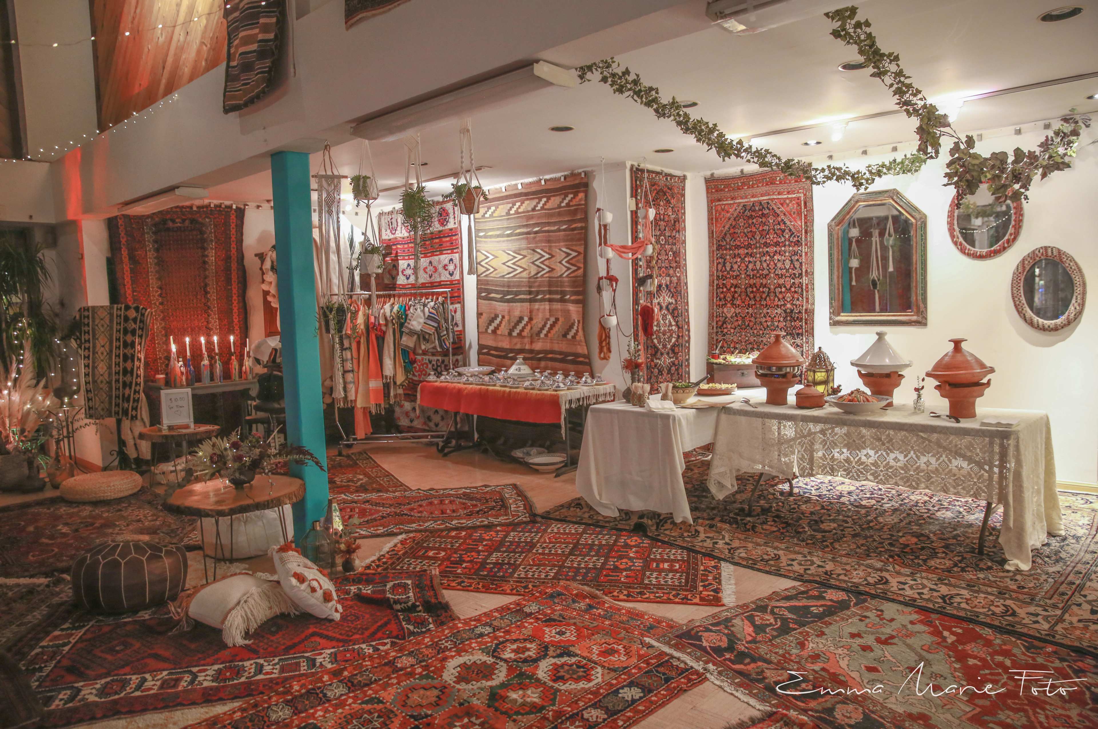The image depicts a cozy room decorated with various colorful rugs, traditional ceramics, and a table set with dishes, all under soft lighting.