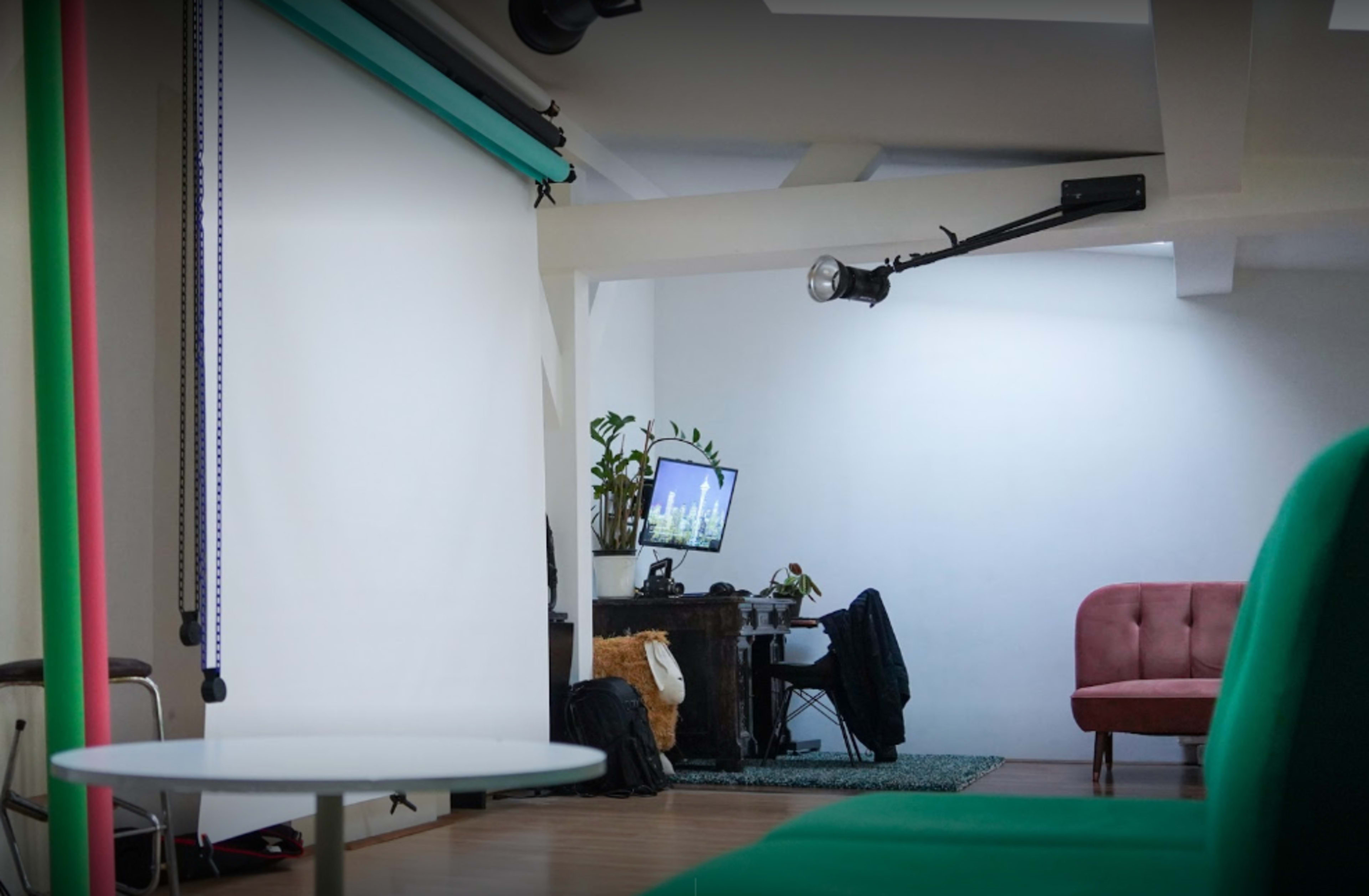 A modern studio space with a green sofa, a large white backdrop, and a computer setup against the wall.