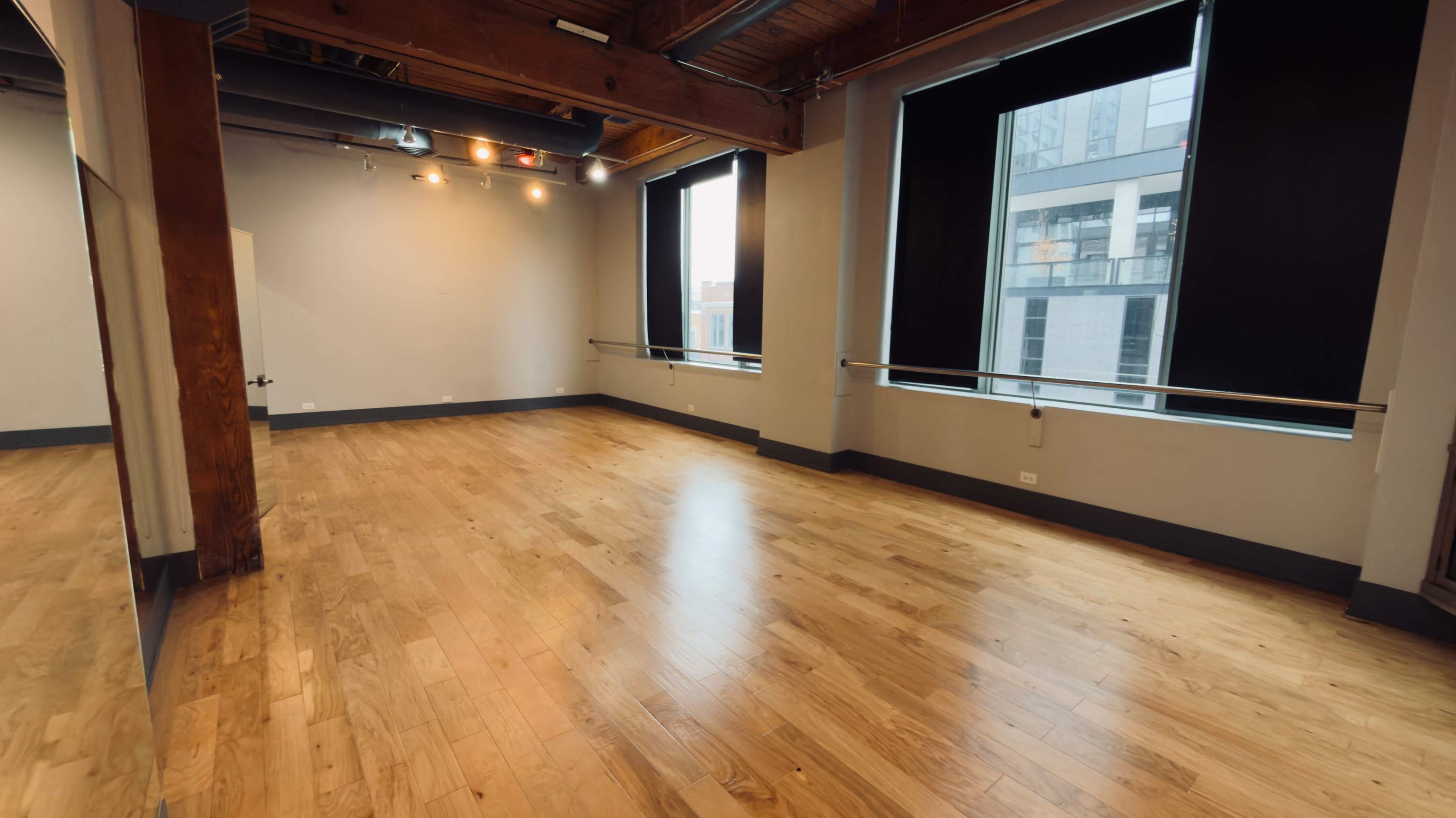 The image shows an empty dance studio with wooden floors, large windows, and exposed wooden beams.