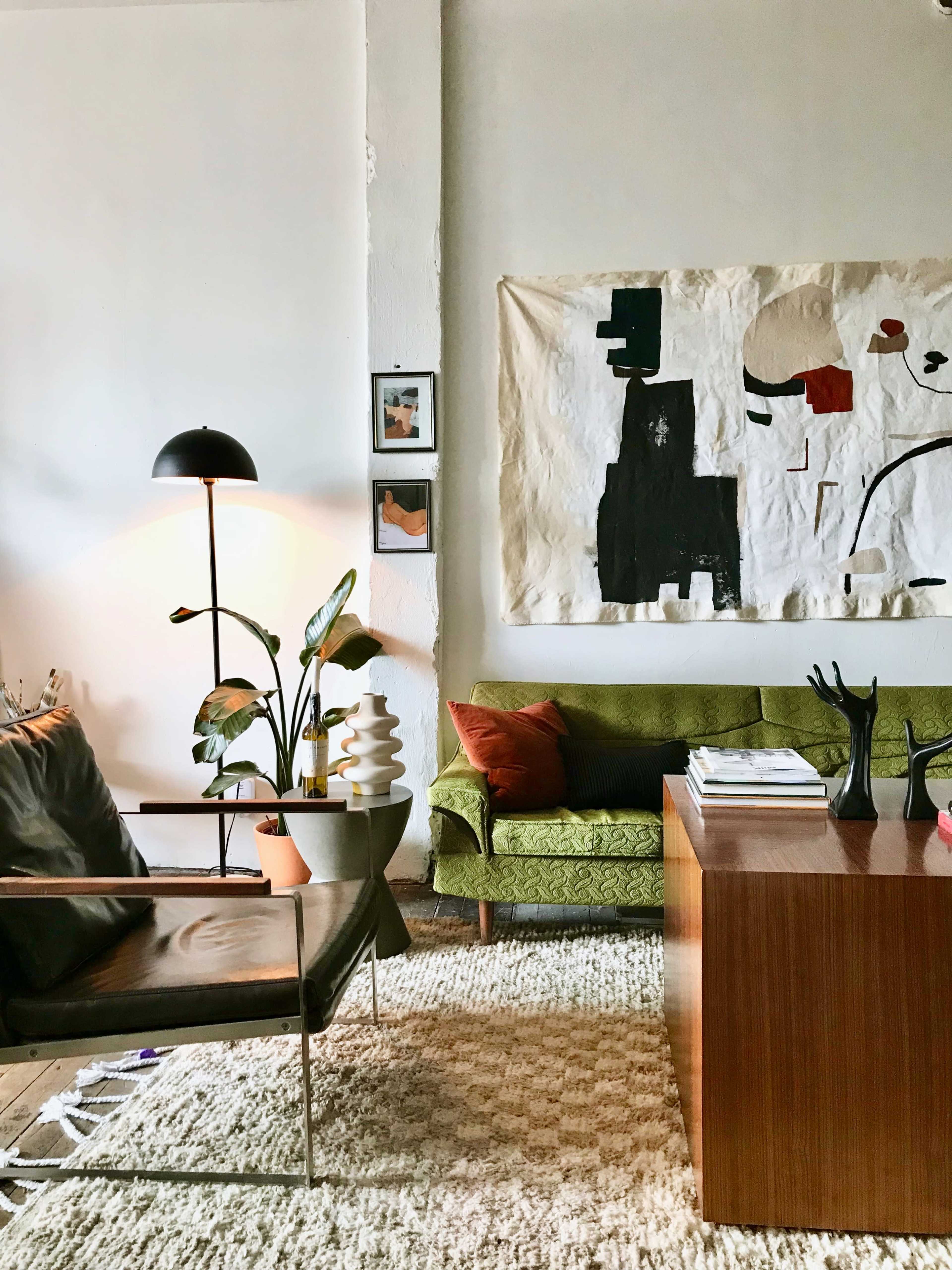 A modern living room with a green couch, a wooden coffee table, a floor lamp, and abstract wall art.