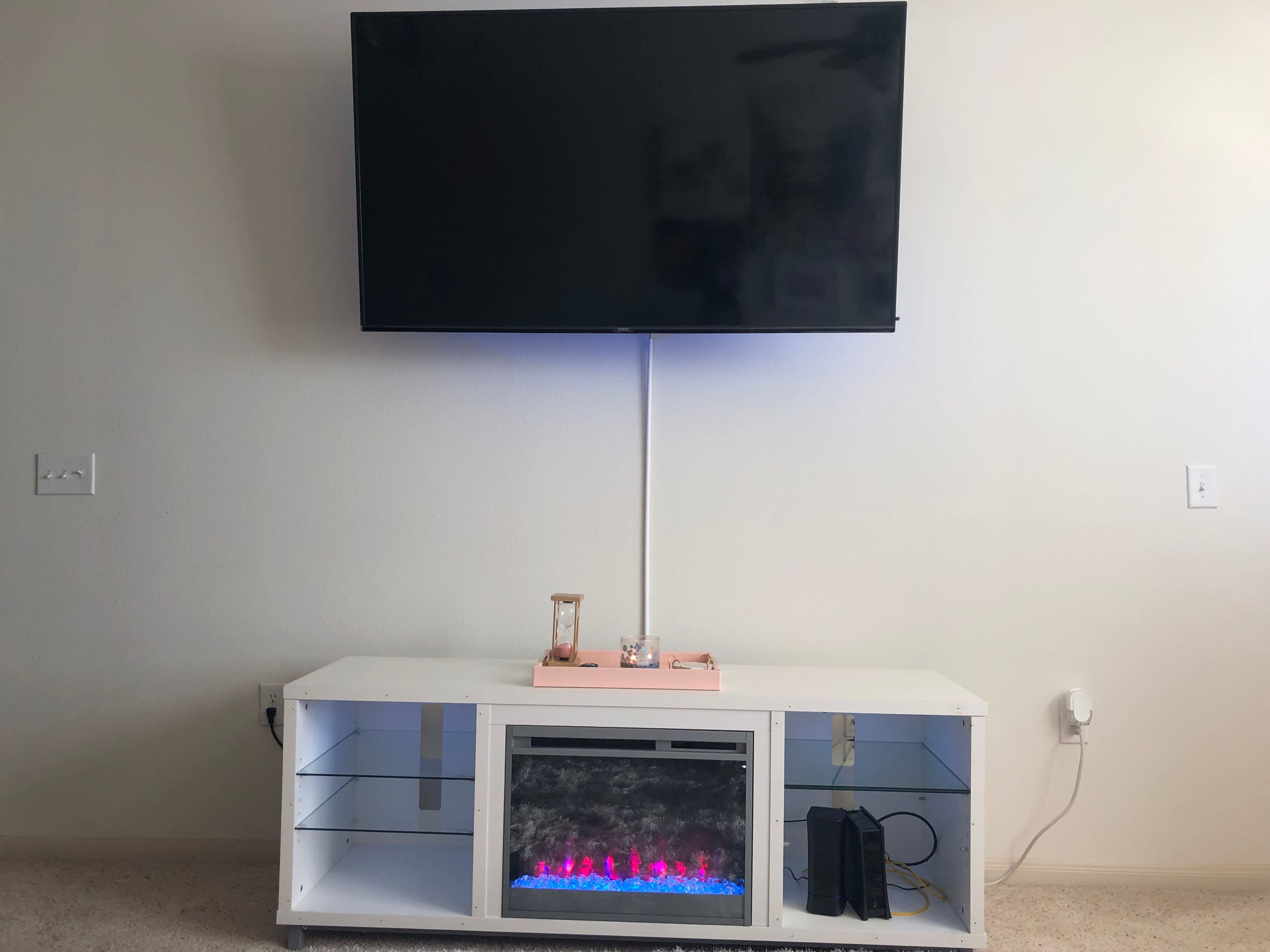 A flat-screen television is mounted above a white entertainment center with a faux fireplace and decorative items.