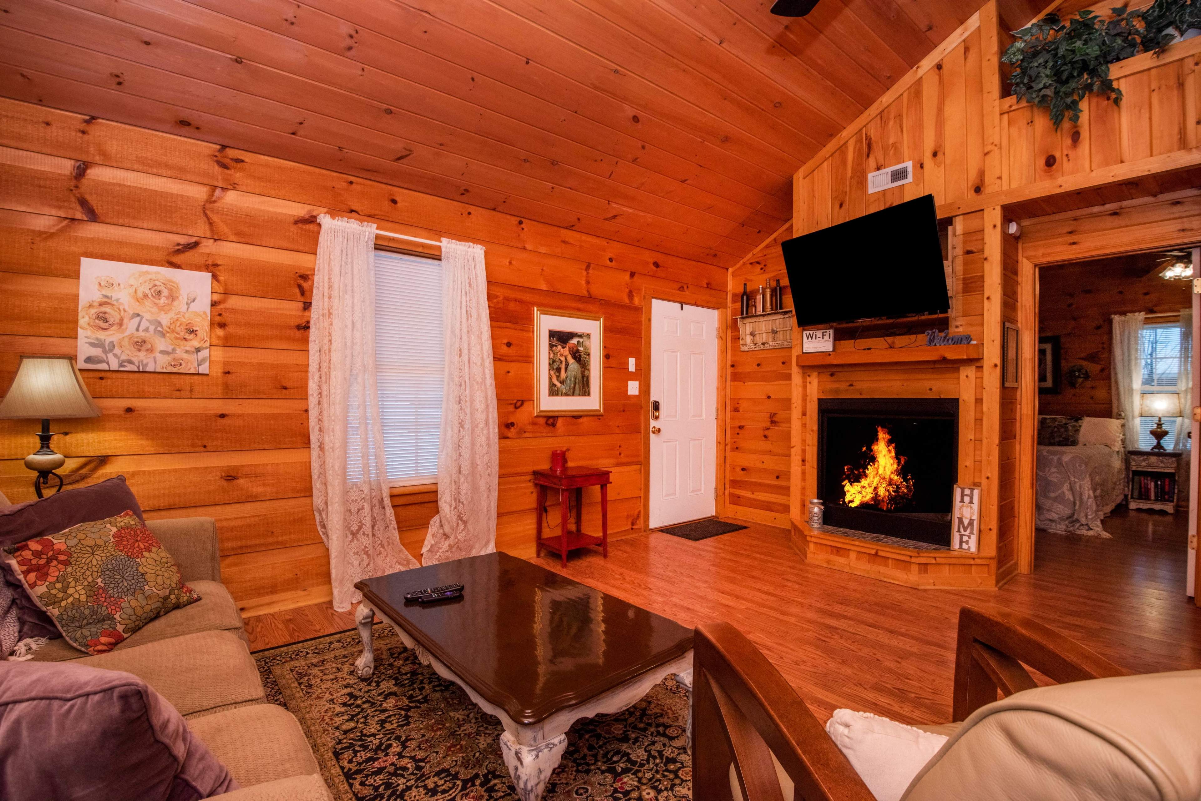 A rustic wooden living room with a sofa, a coffee table, and a fireplace with an artificial flame.