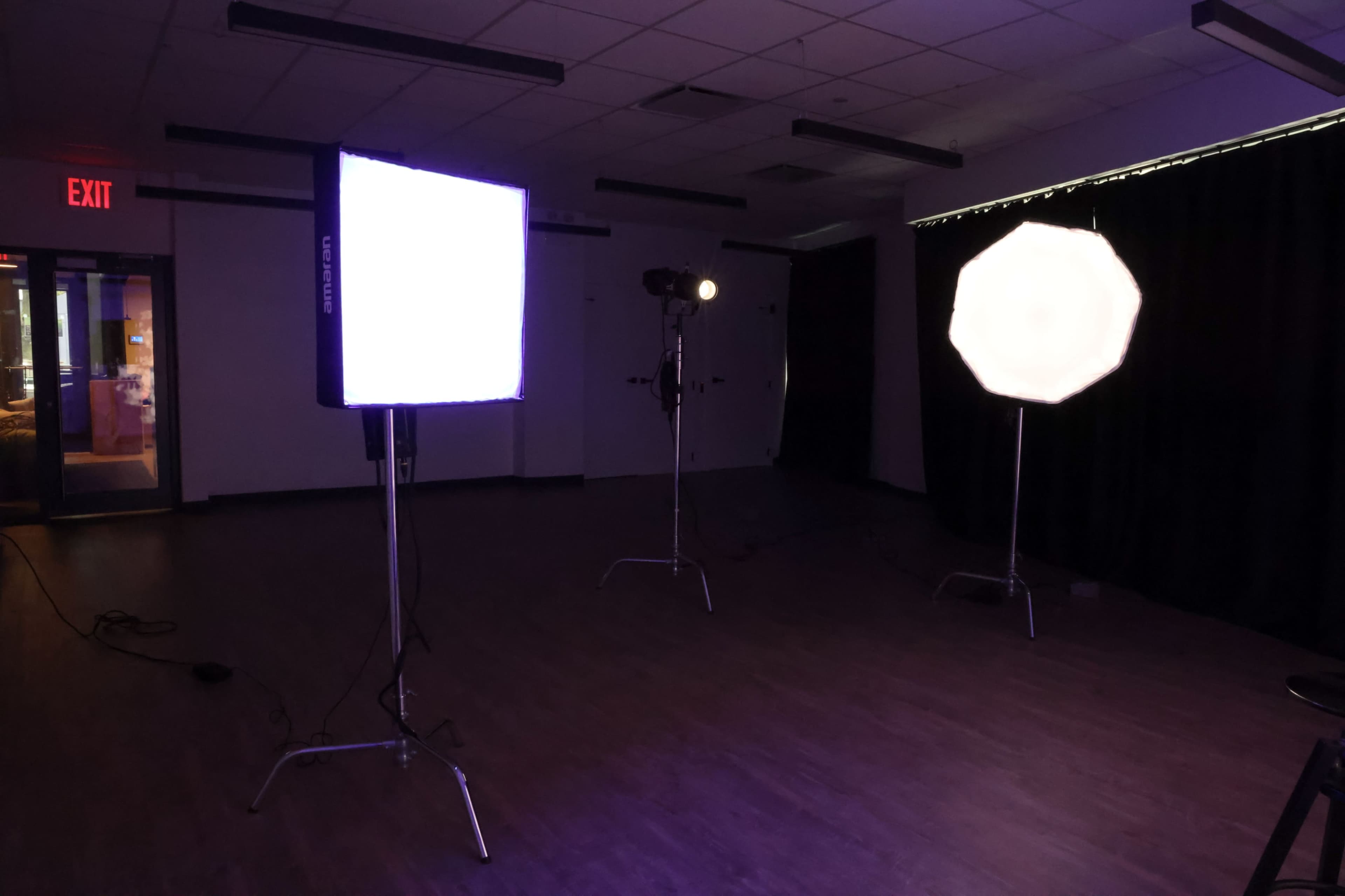 The image shows a dimly lit studio with three lighting setups, including a softbox and an LED panel.