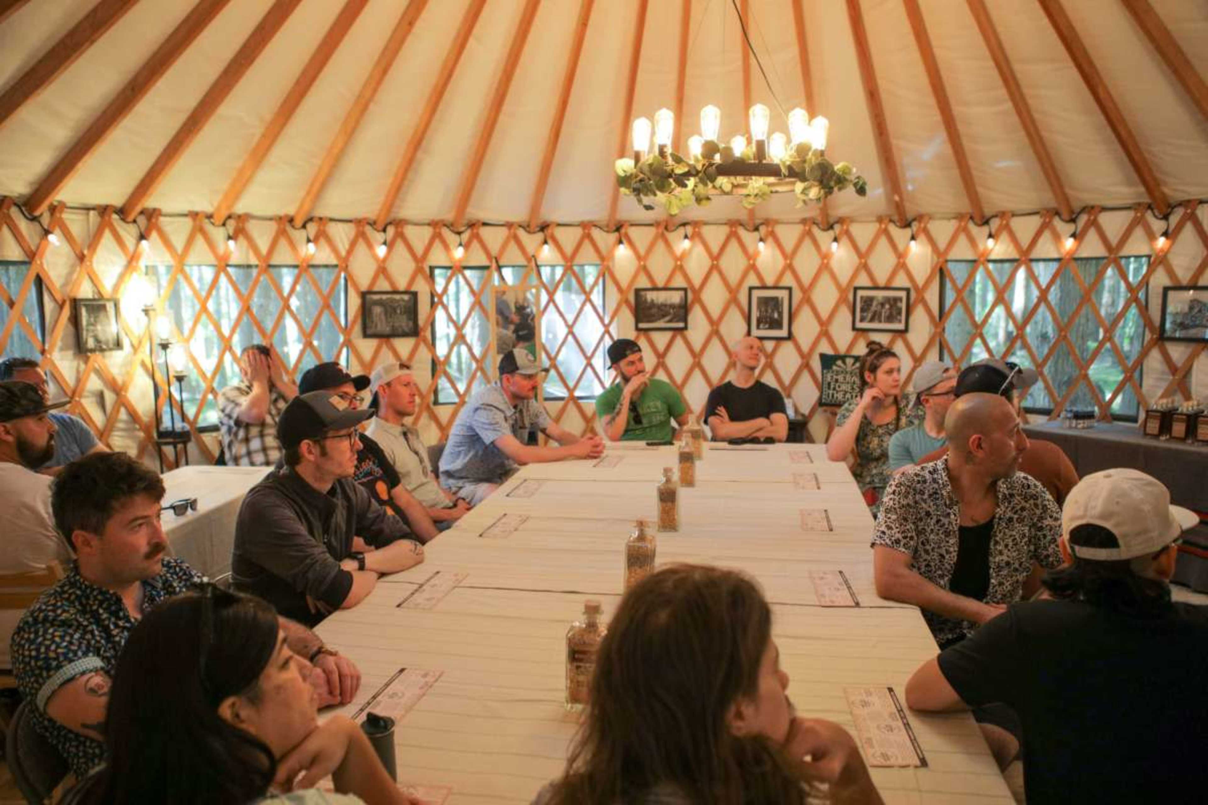 A group of people sits around a long table inside a yurt, with various photographs hanging on the walls.