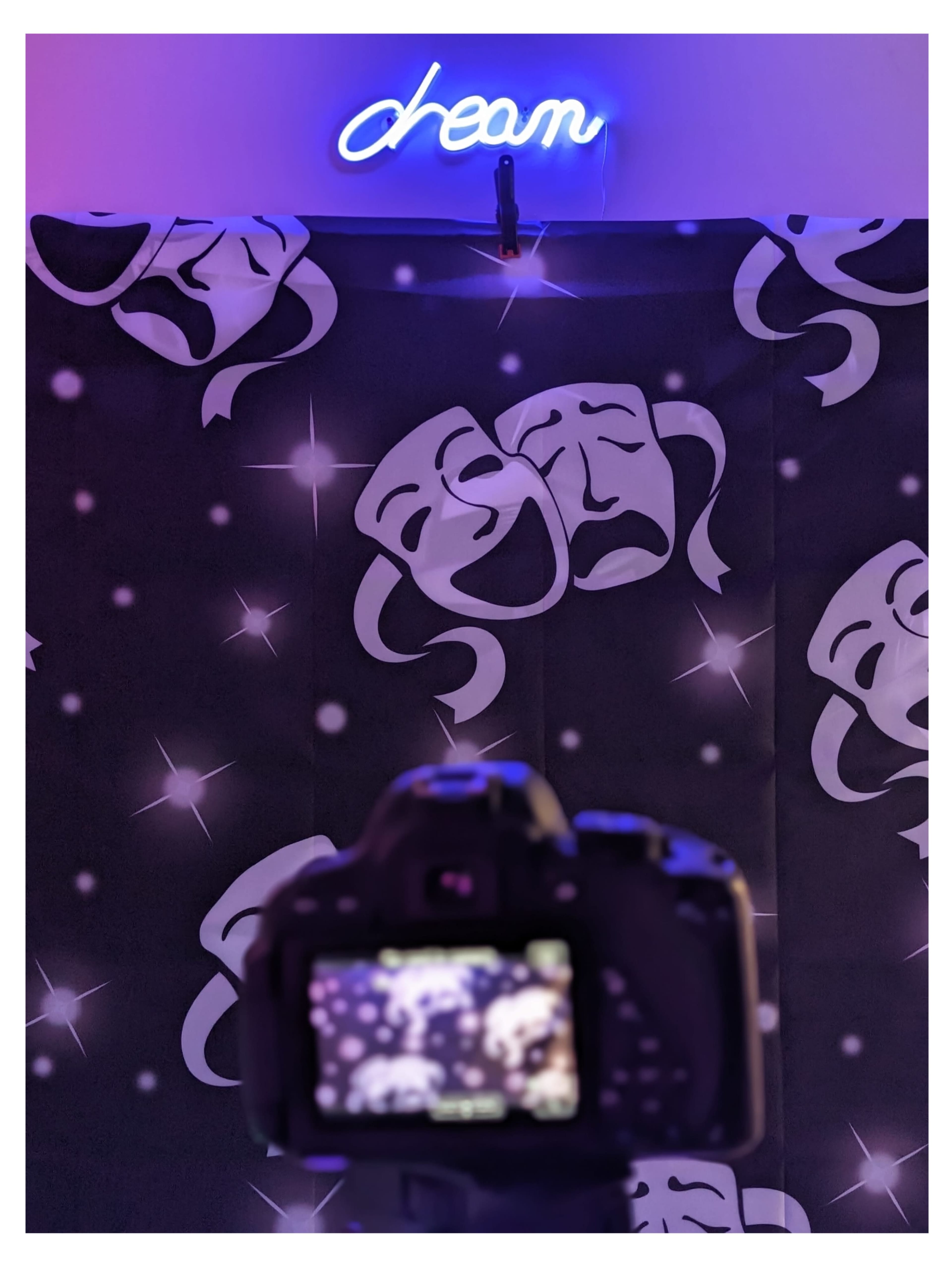 A camera focuses on a backdrop featuring theatrical masks and a neon sign that reads "dream."