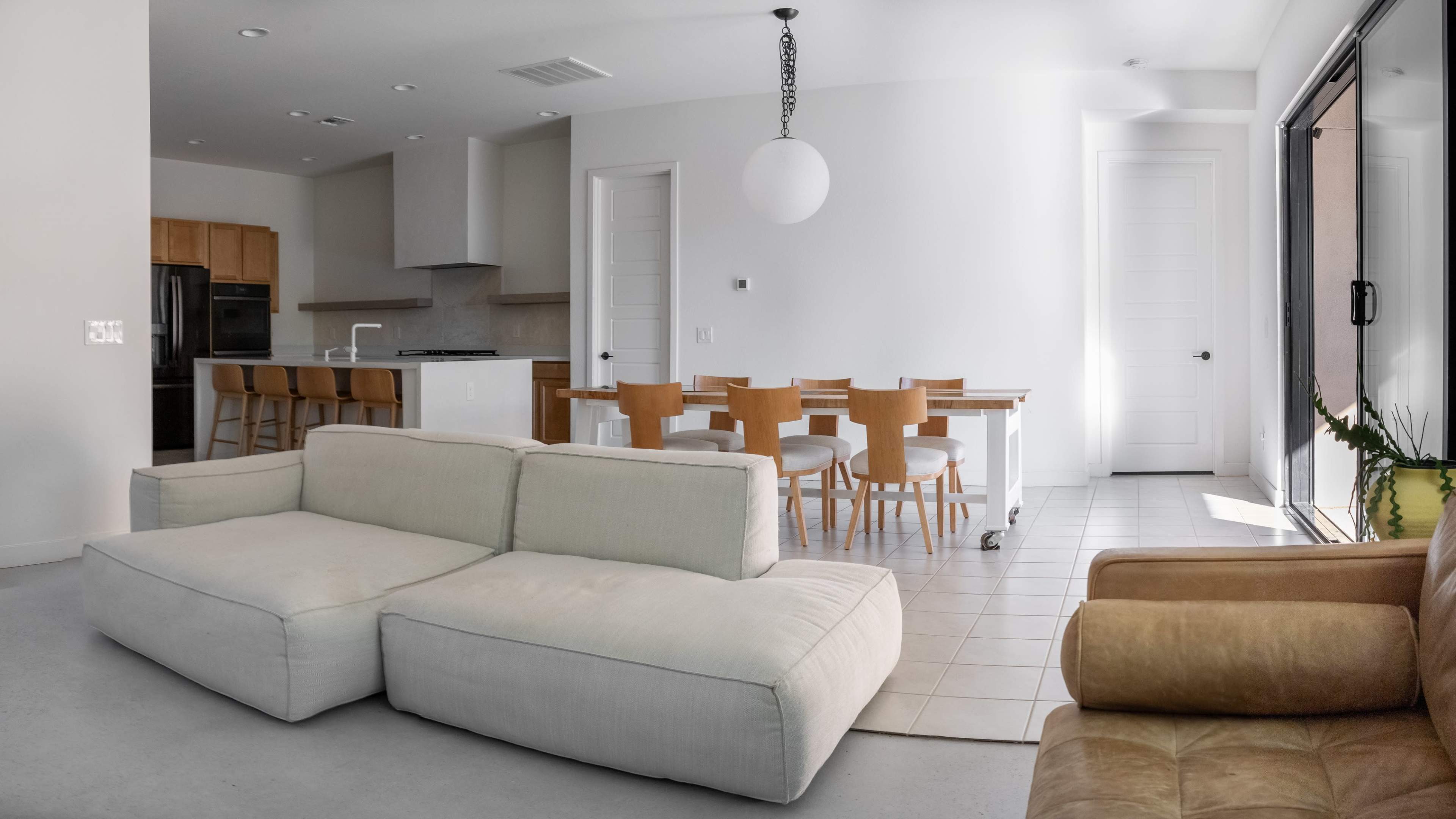 A modern living space with a white sofa and a brown leather chair, overlooking a dining area equipped with a wooden table and chairs.