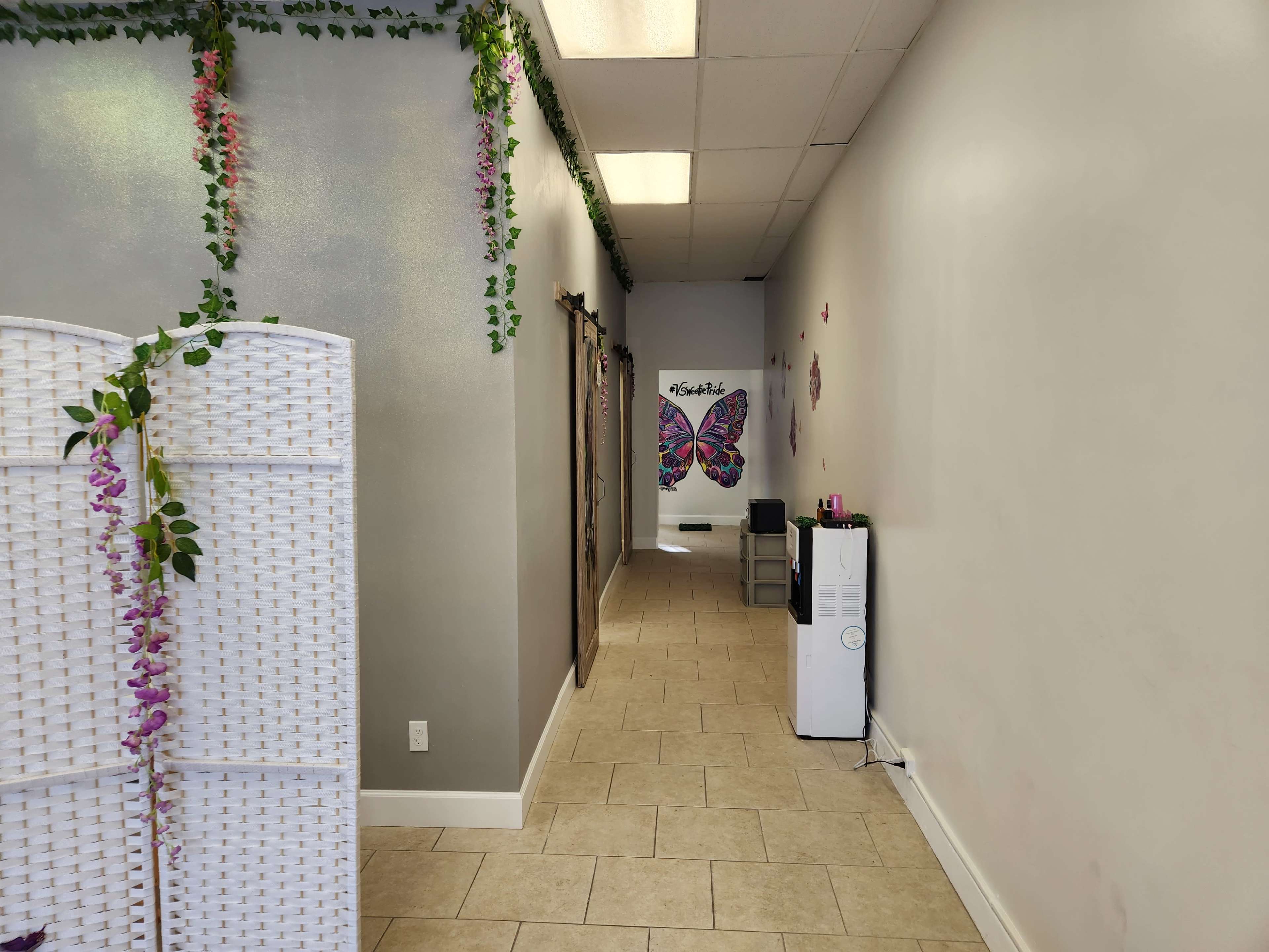 A hallway with light-colored tiled flooring, decorated with greenery and a butterfly mural at the far end.