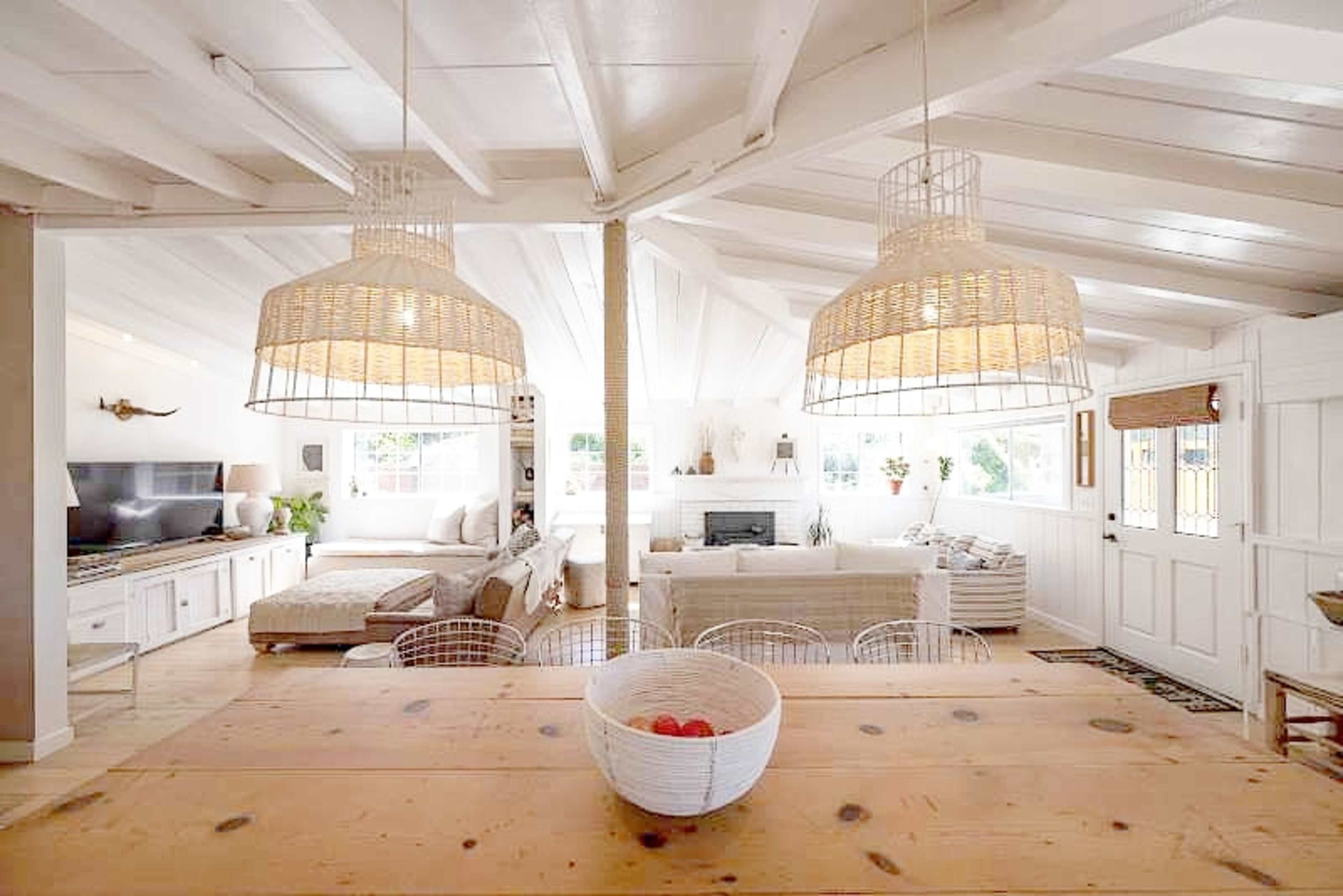 A light-filled, open-concept living space featuring a dining area with a wooden table and wicker pendant lights over a cozy seating area.