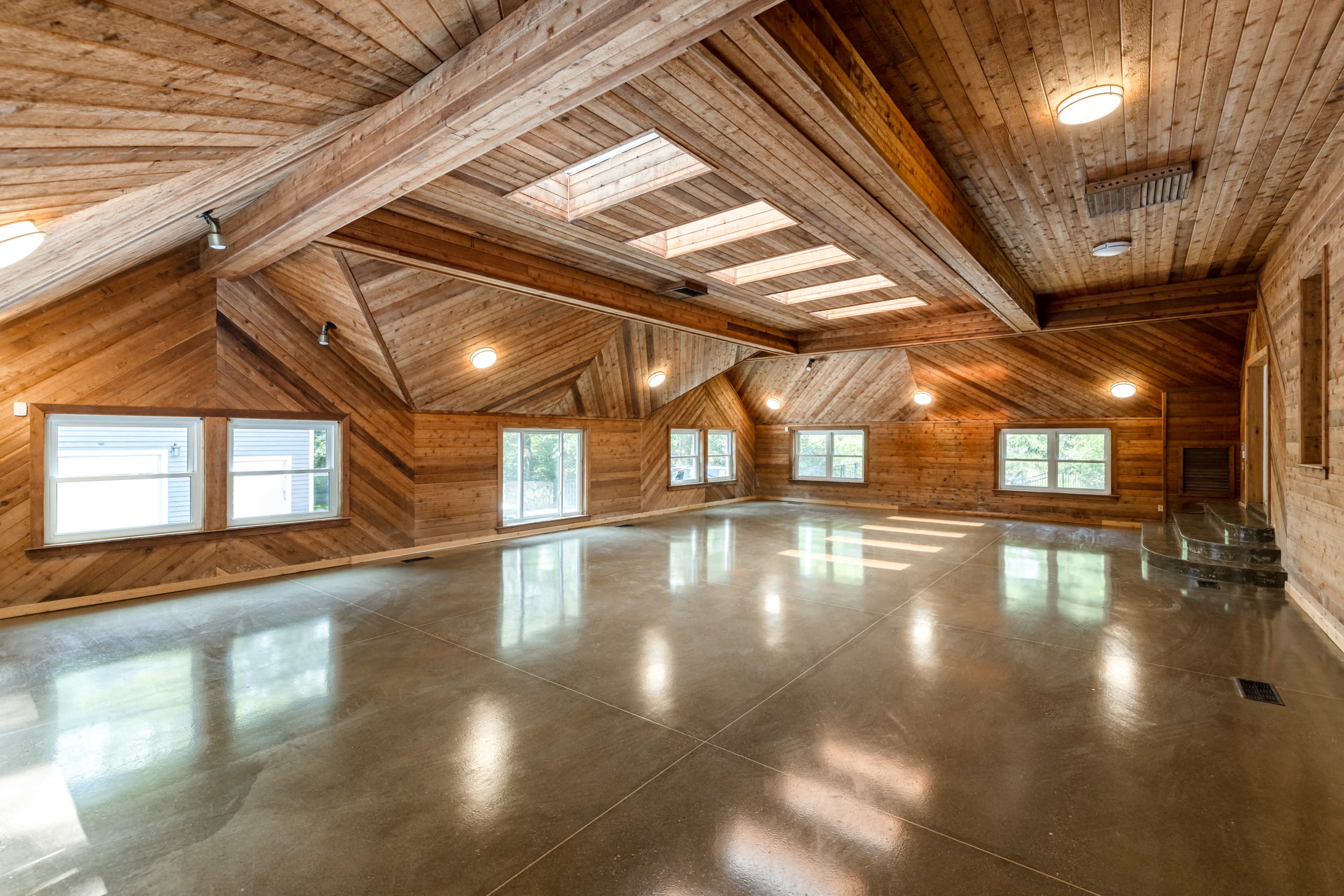 A spacious interior with wooden walls and ceilings, large windows, and a polished concrete floor.