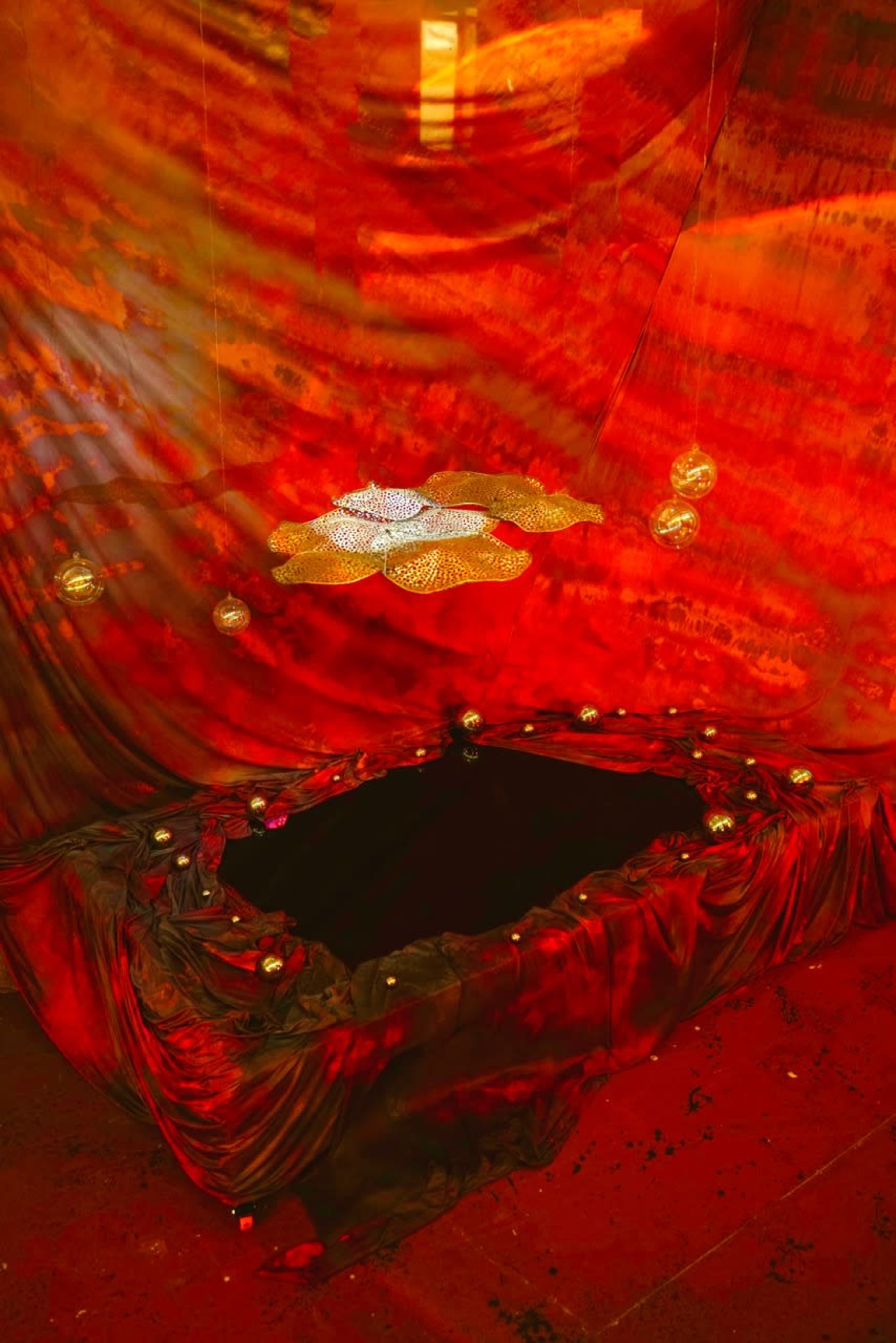 The scene features a dark, elongated space draped in red fabric with decorative elements hanging above.
