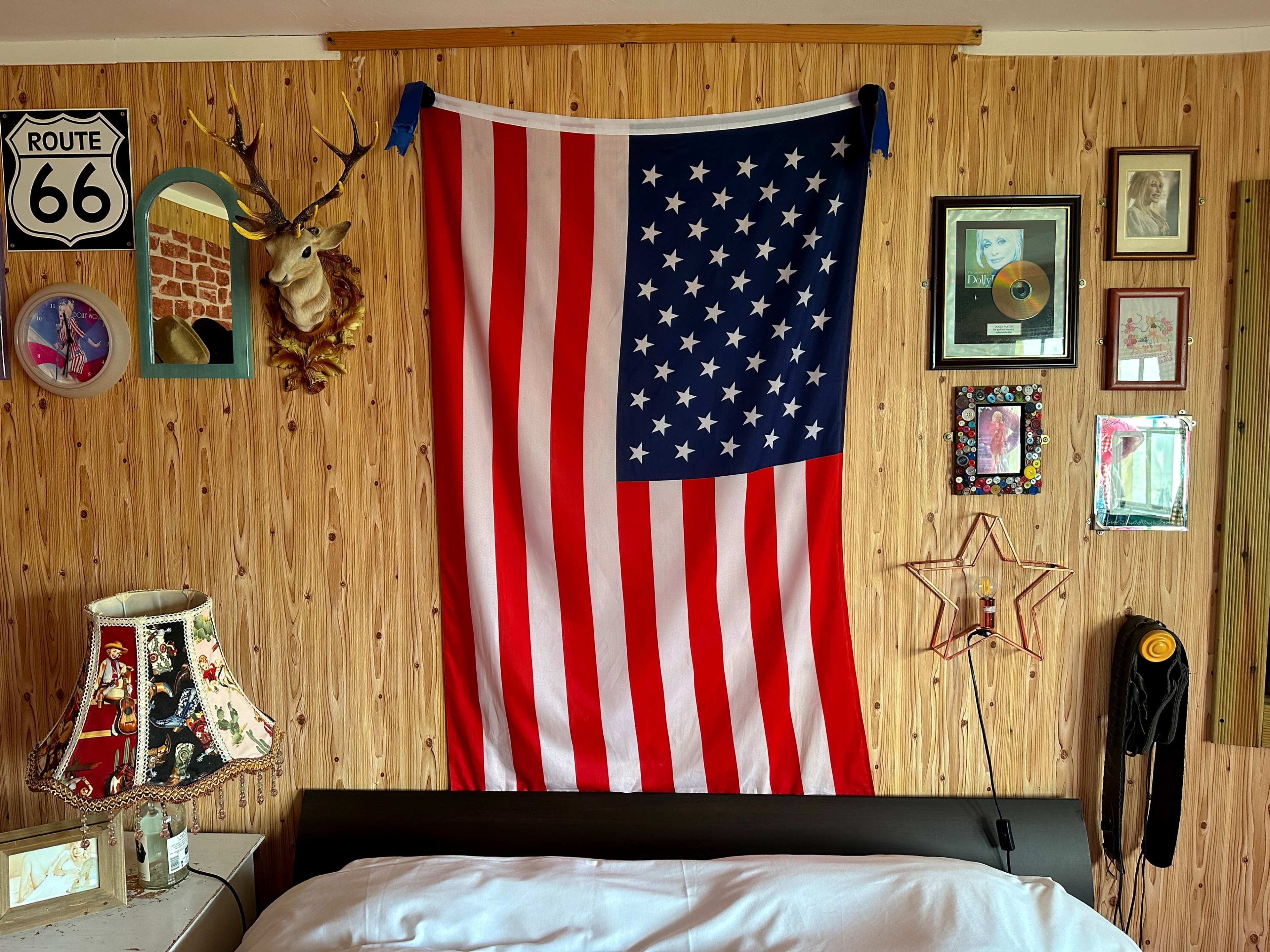 A large American flag hangs on the wall of a room decorated with vintage photographs, a deer head mount, and a Route 66 sign.