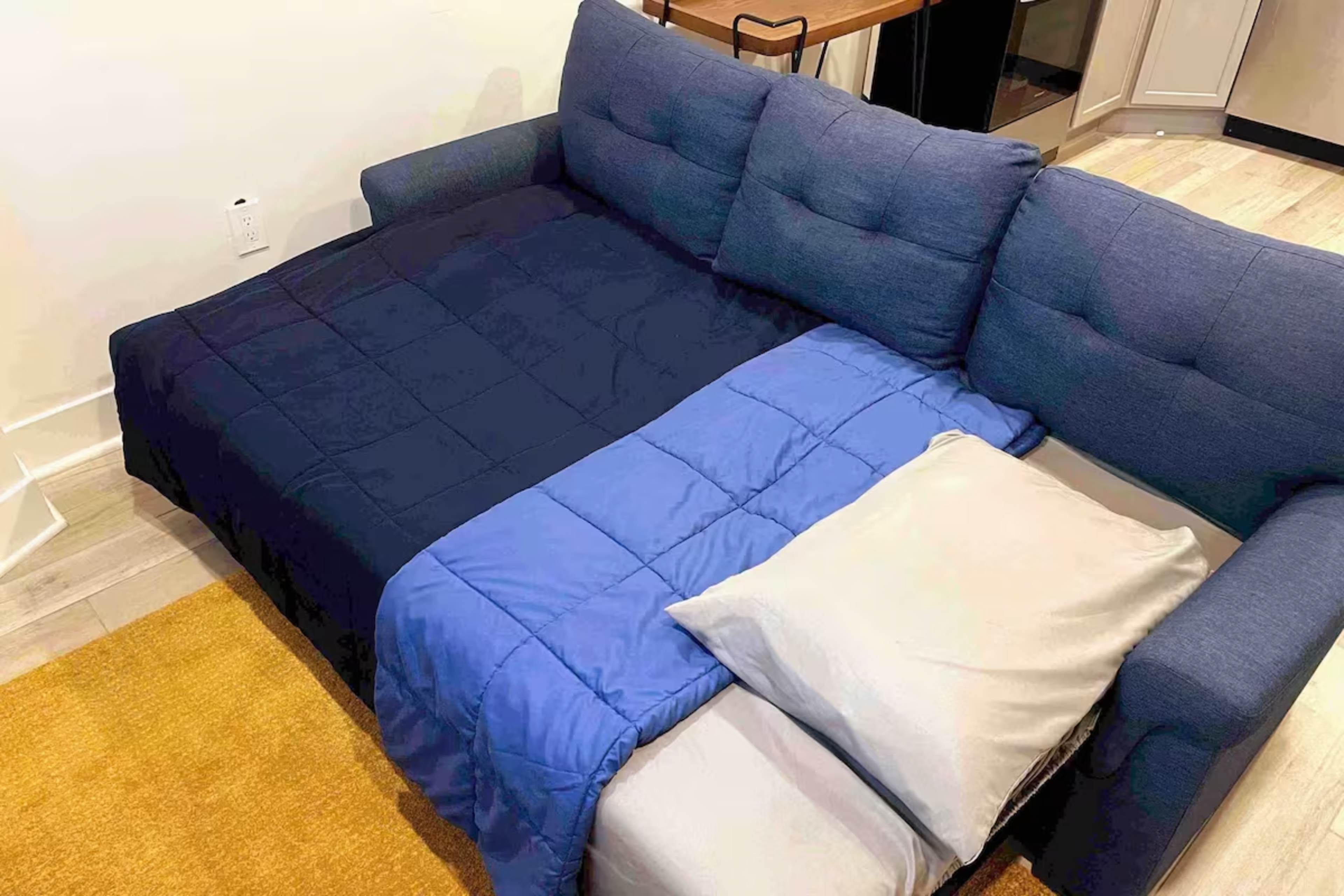 The image shows a blue couch with a folded blanket and two pillows arranged on it.
