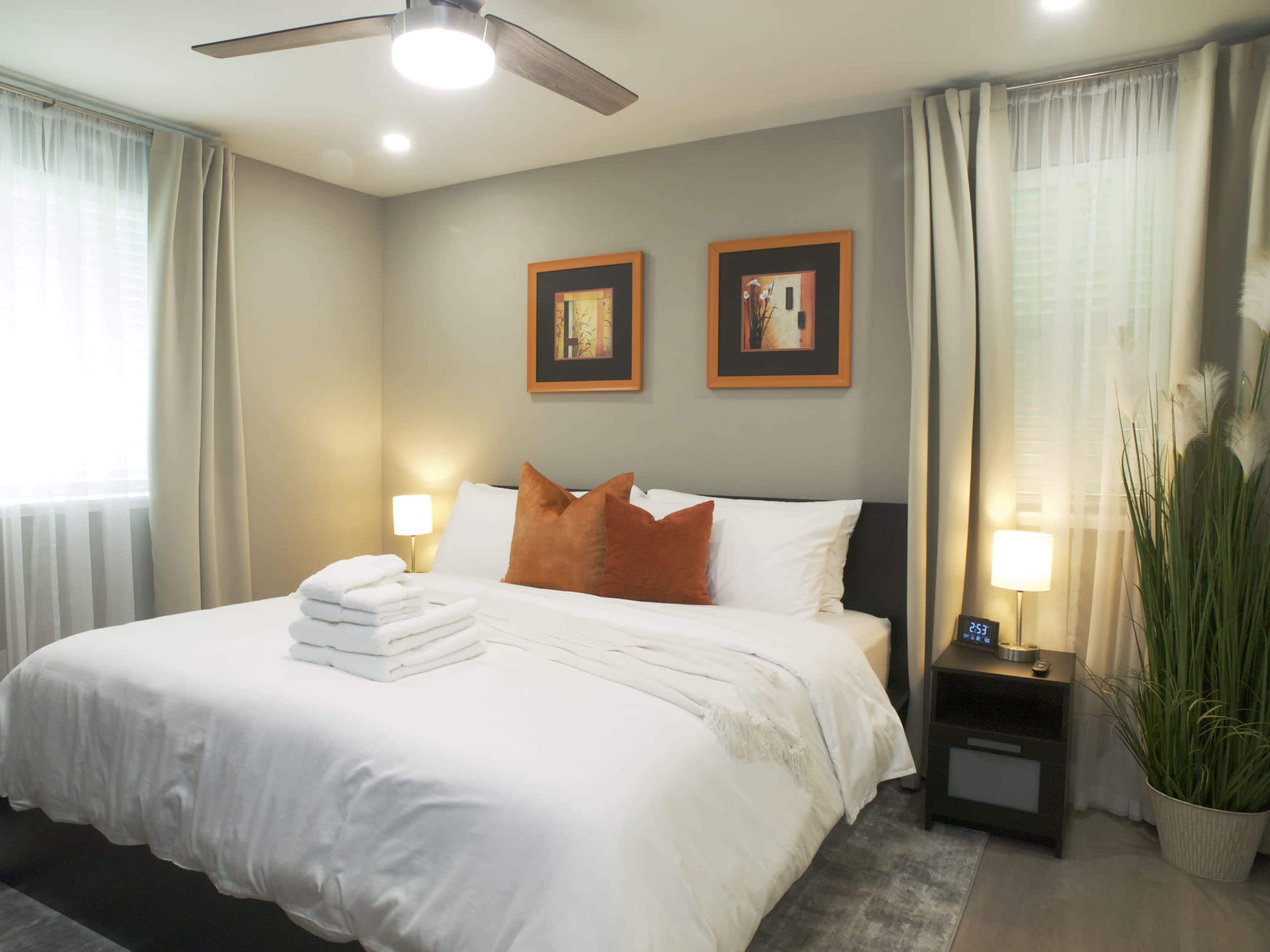 A neatly arranged bedroom featuring a large bed with white linens, decorative pillows, a nightstand with a clock, and framed art on the walls.