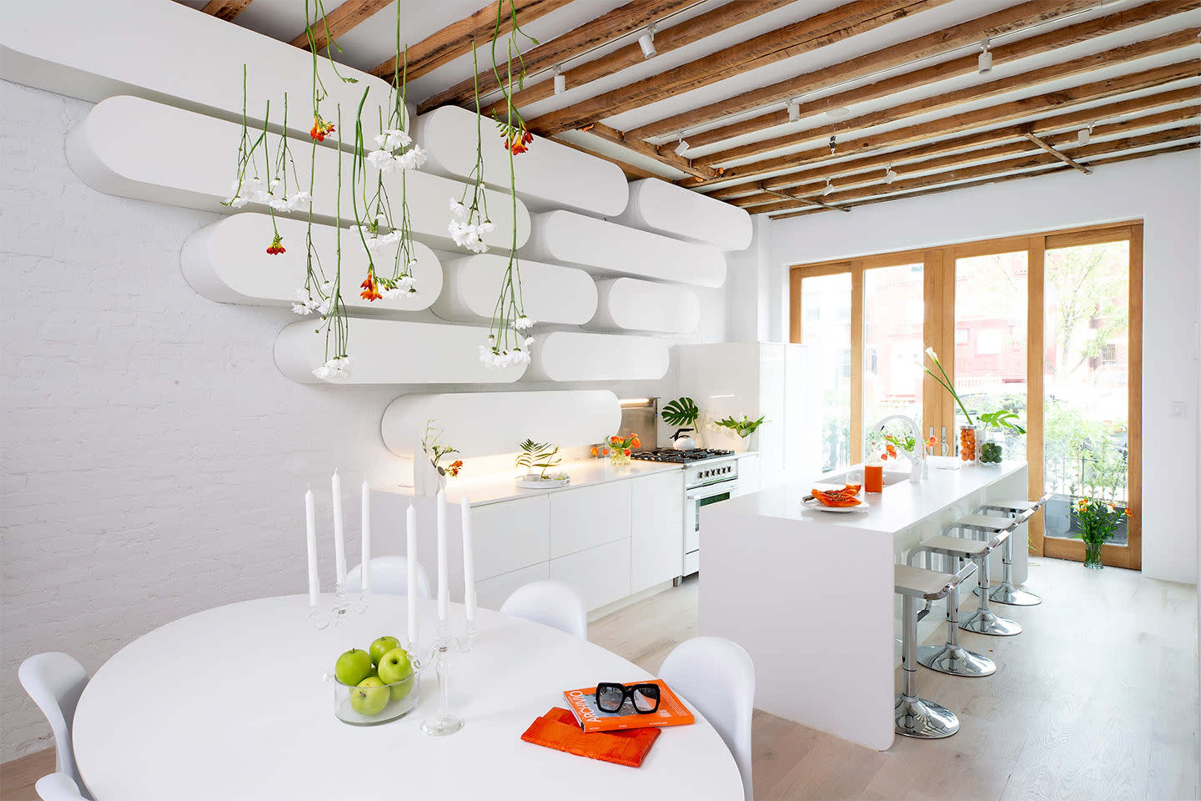 A modern kitchen features a minimalist design with a round dining table, white cabinetry, and floating shelves adorned with plants.