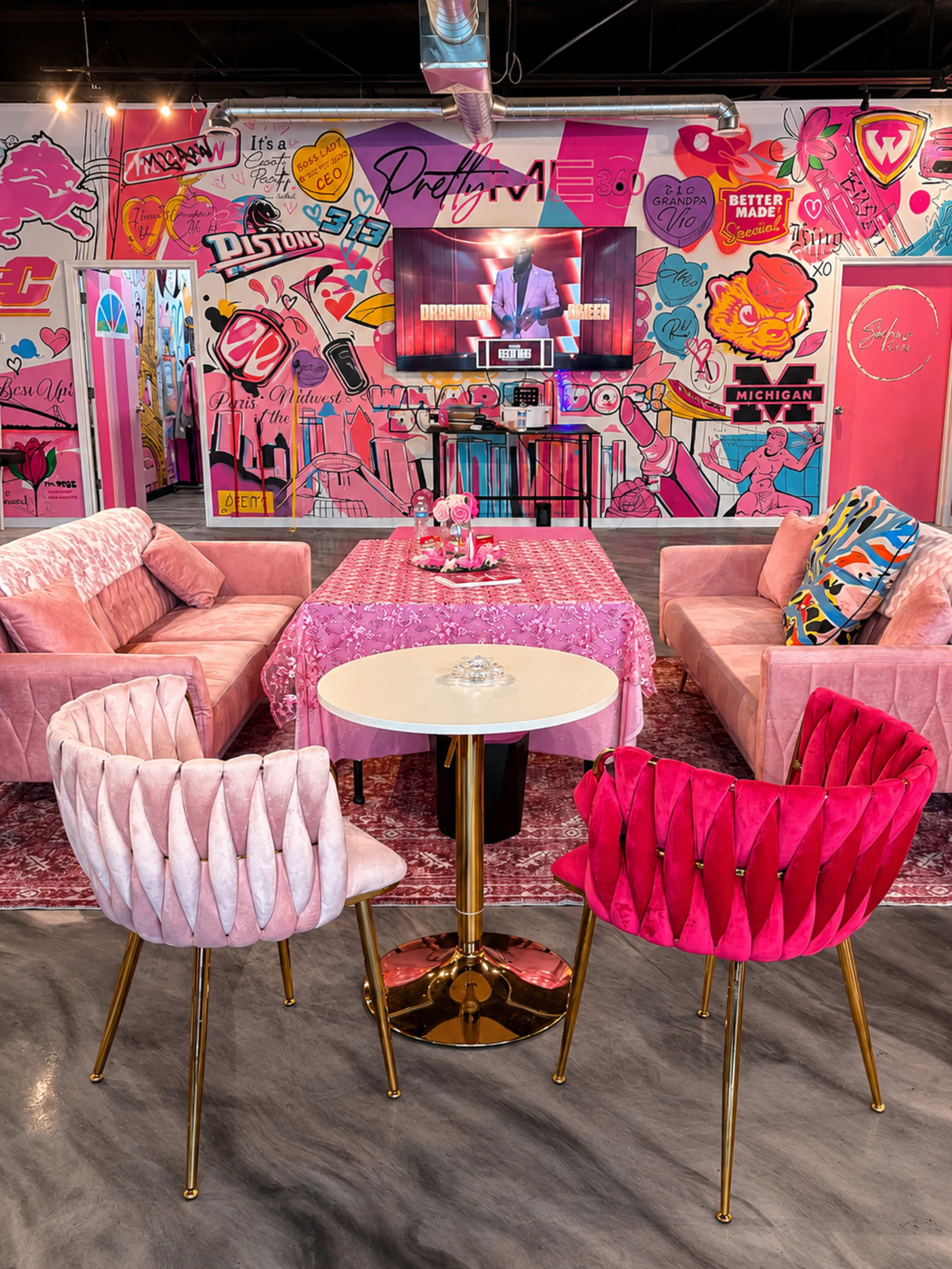 The image features a vibrant lounge area with pink upholstered sofas, stylish seating, and a colorful mural in the background, all centered around a television screen displaying a program.