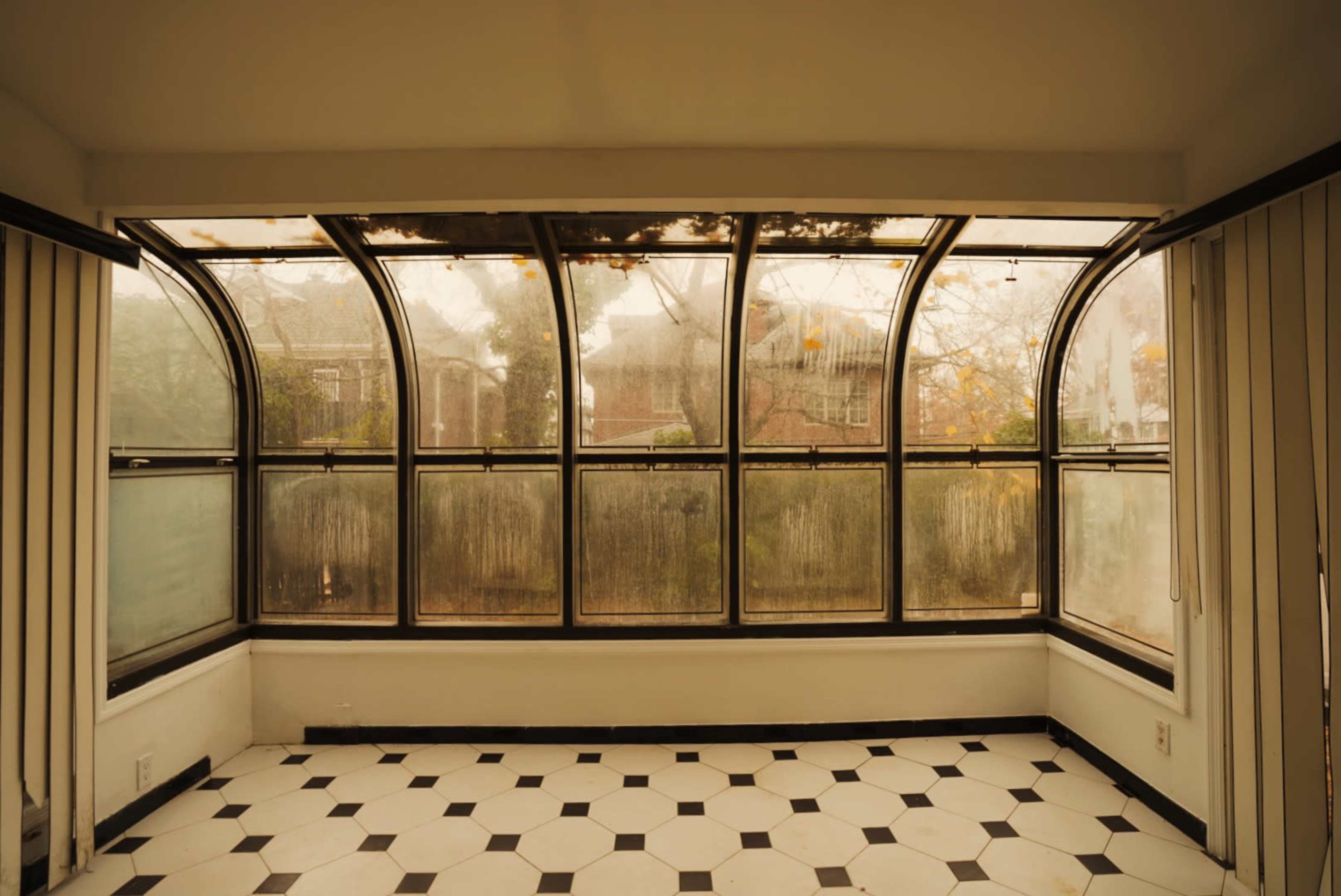 A sunroom with large curved windows, featuring fogged glass and a patterned black and white tiled floor.