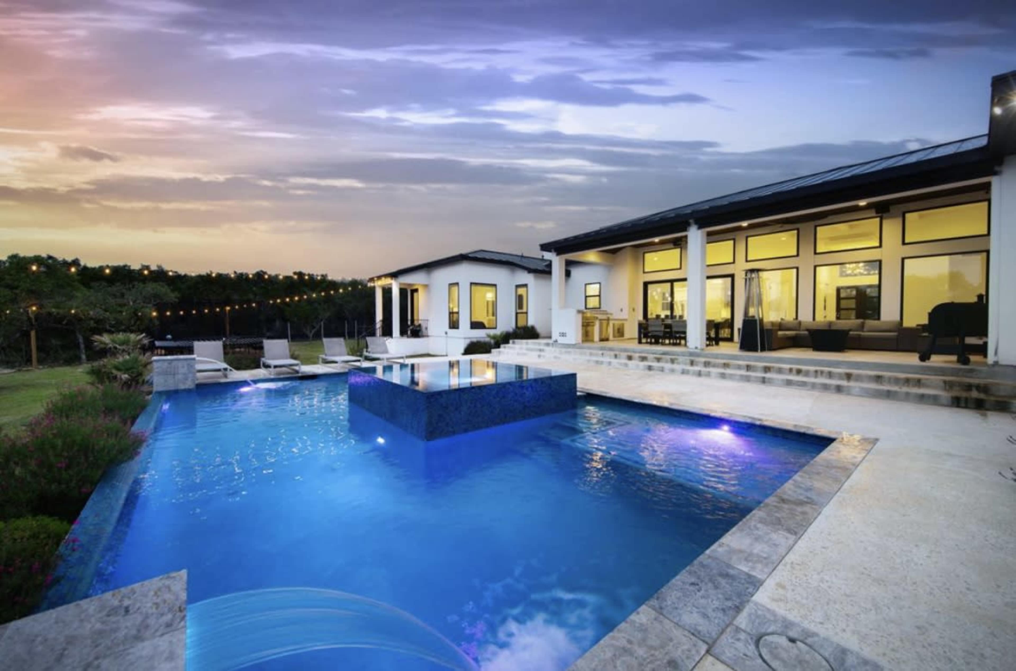 A modern house with a large swimming pool and an outdoor seating area is set against a twilight sky.