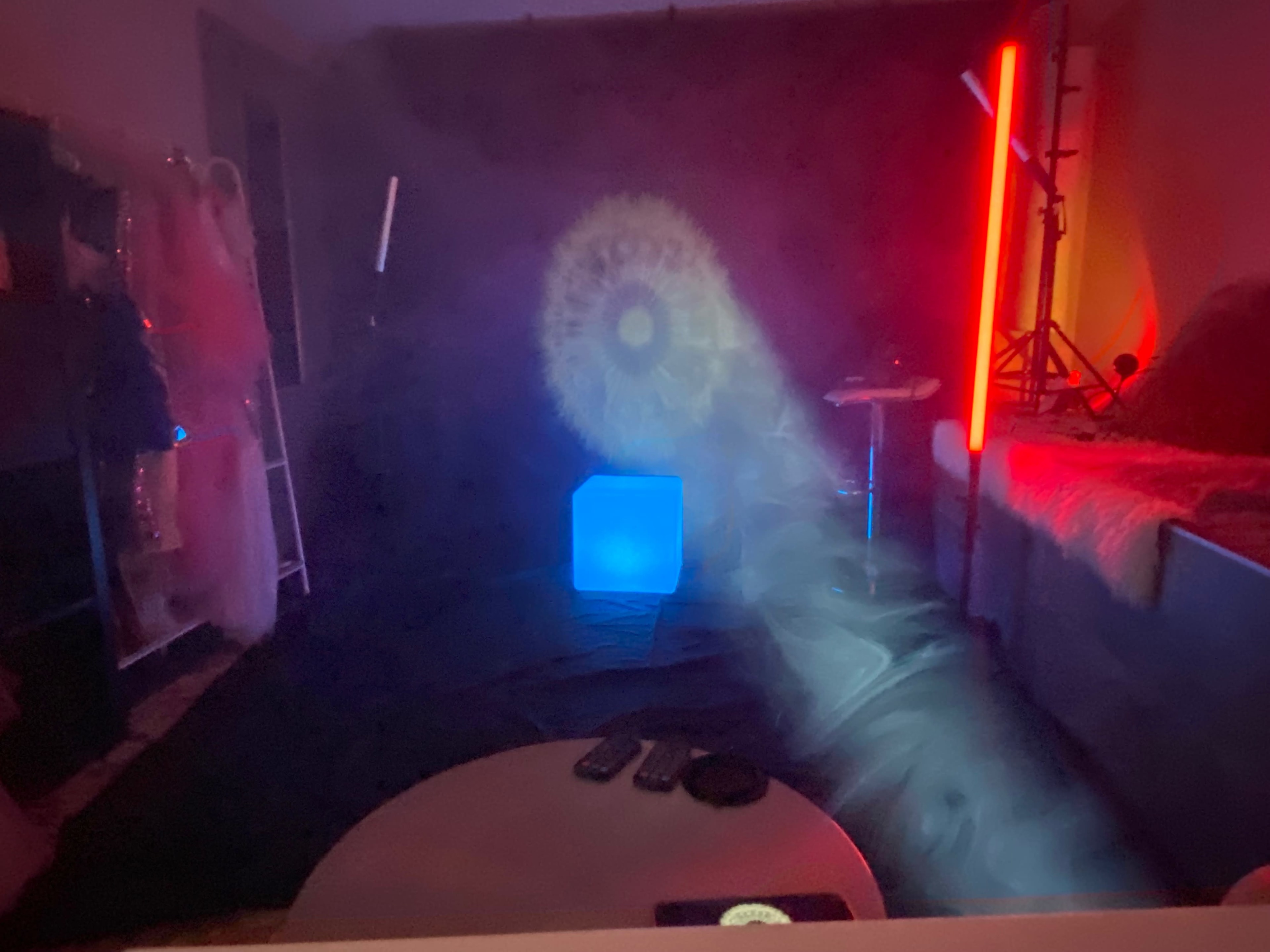 A dimly lit room with a blue illuminated cube on the floor, surrounded by colorful lighting and smoke effects.