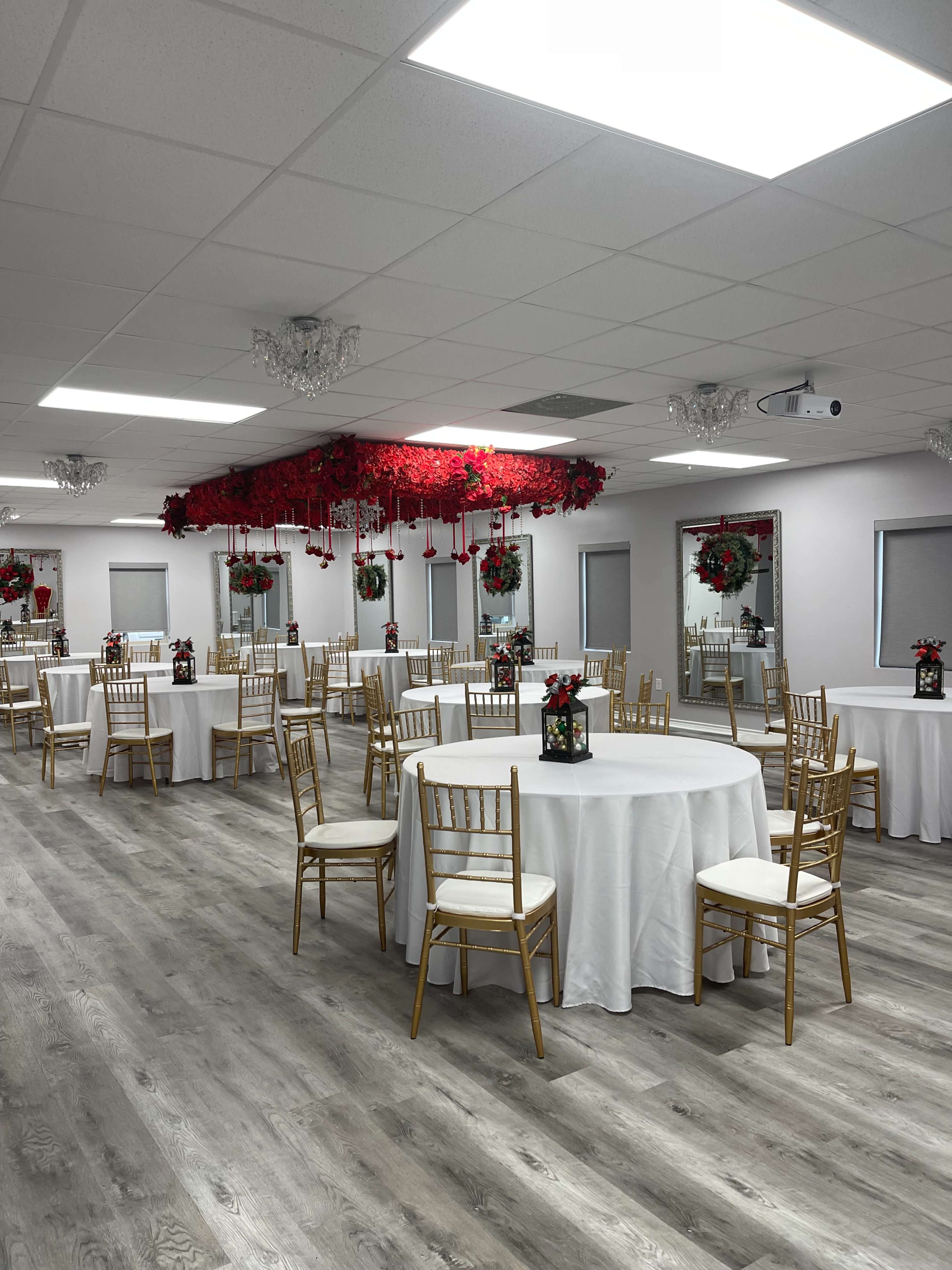 A decorated event space with round tables, gold chairs, and floral arrangements hanging from the ceiling.