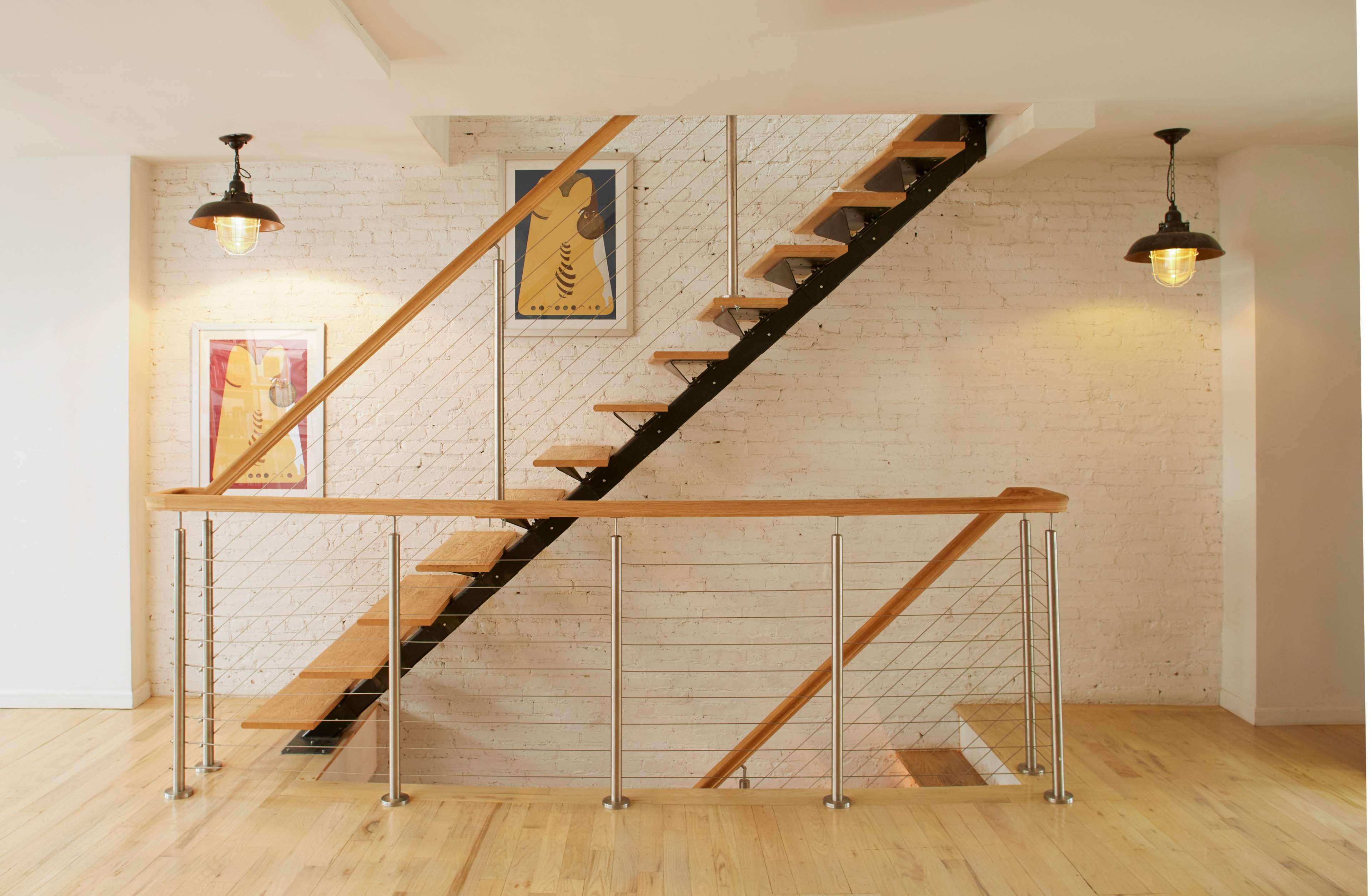 A modern staircase with wooden steps, a metal railing, and framed artwork on the walls in a well-lit space.
