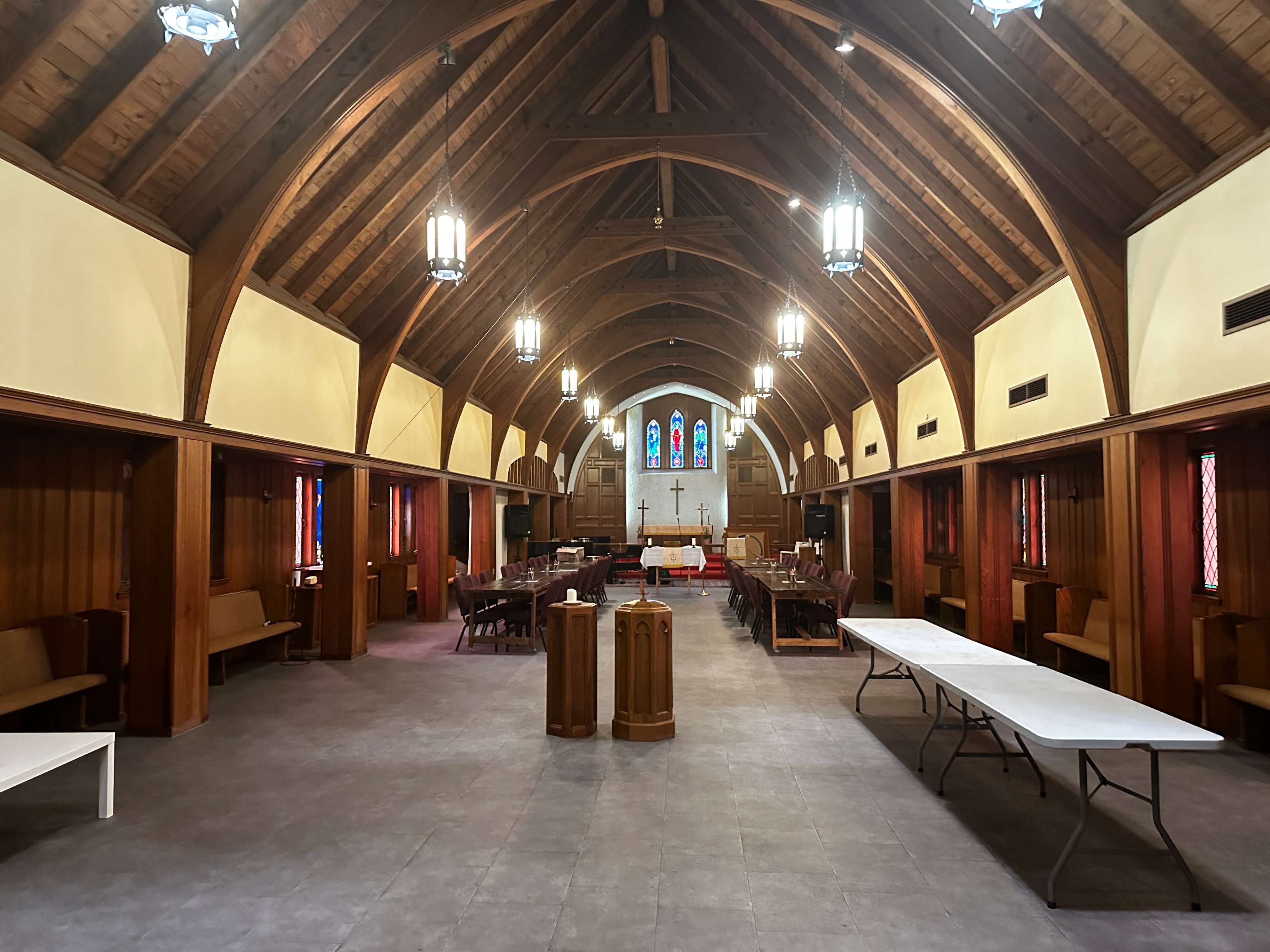 The interior of a church with a vaulted wooden ceiling, rows of seating on either side, and stained glass windows at the far end.