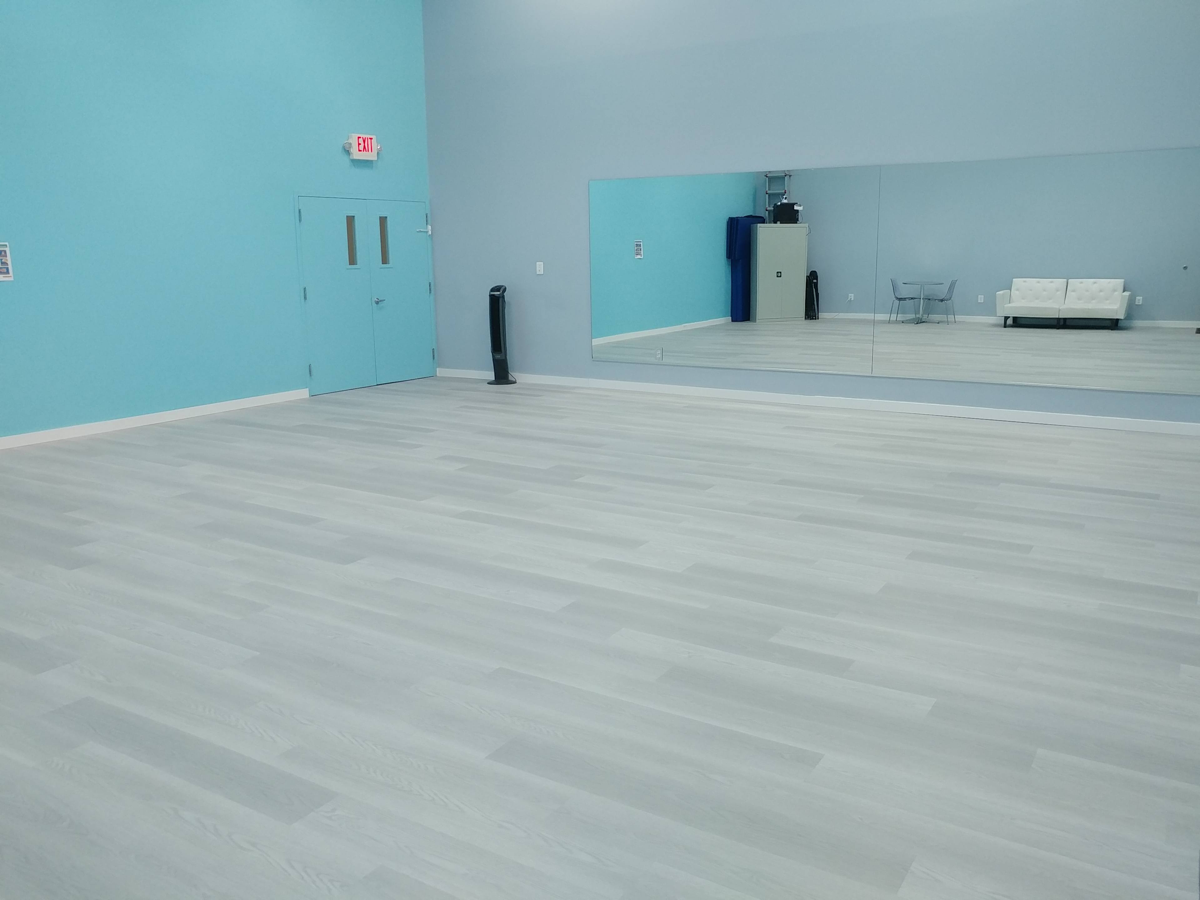 A spacious room with light gray flooring, light blue walls, a large mirror on one side, and a couch against the wall.