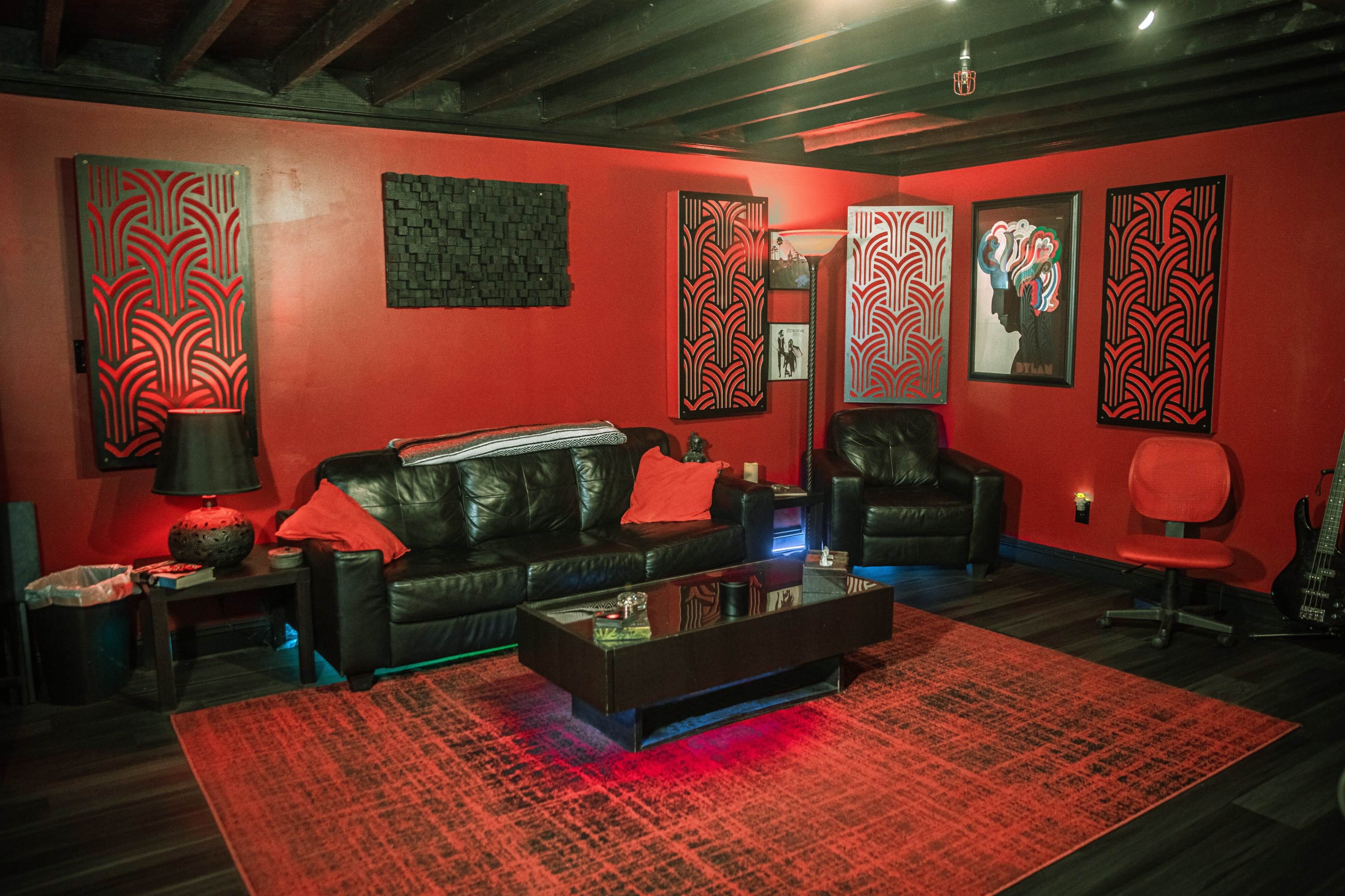 A modern living room with red walls, black leather furniture, and decorative artwork on the walls.