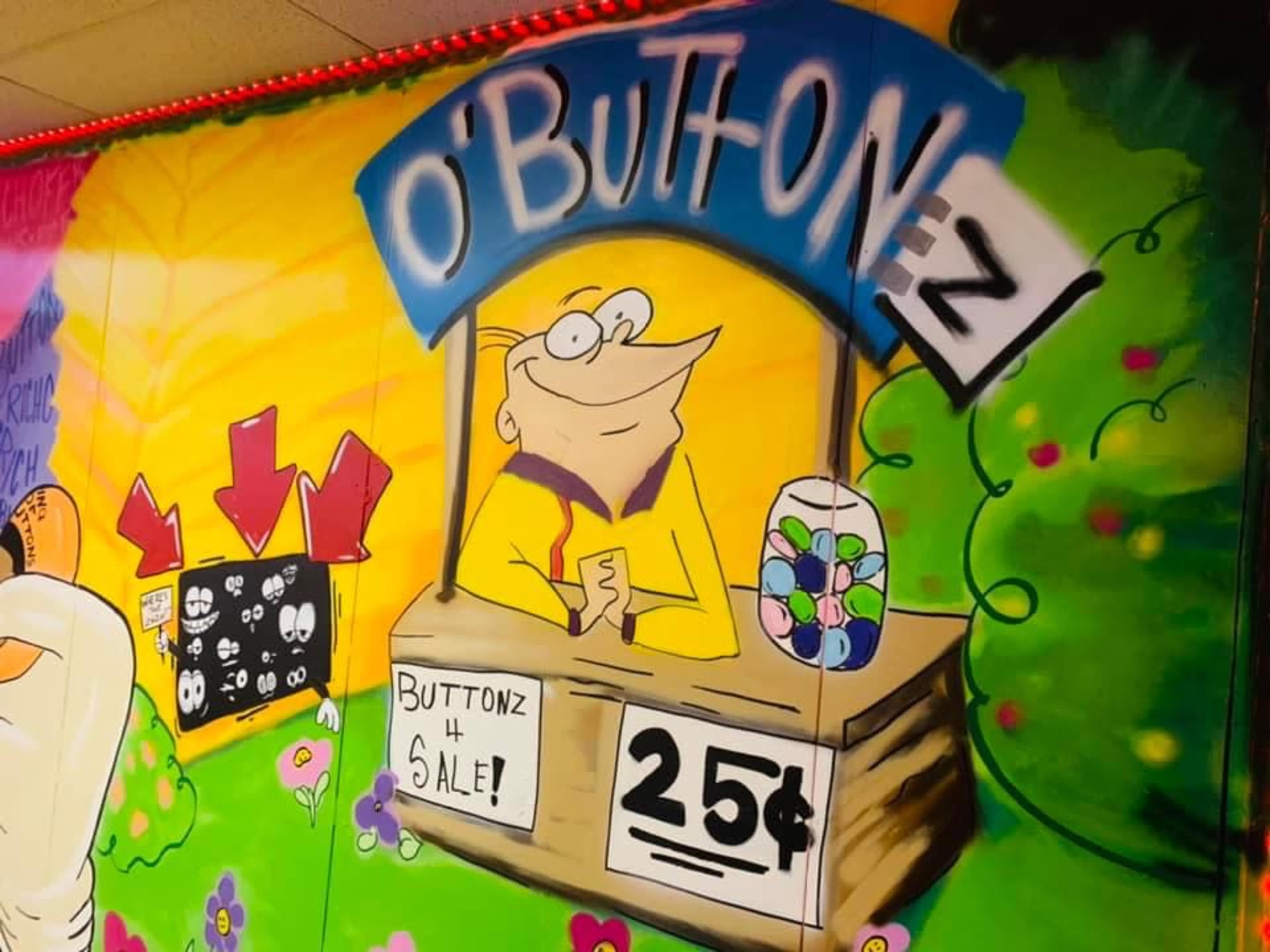 A colorful mural depicts a cartoon character selling buttons at a stand labeled "O'Buttonz" for 25 cents.
