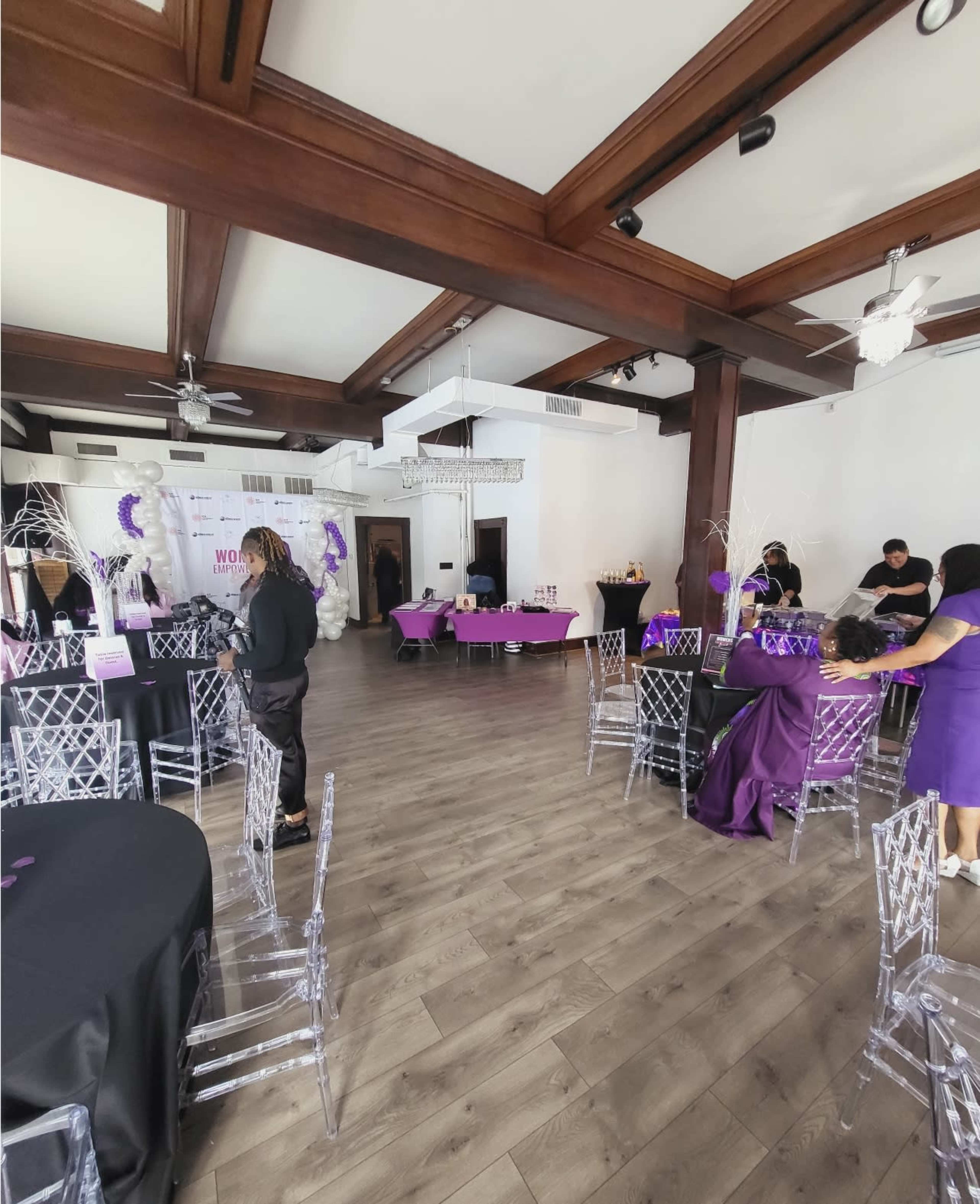A spacious event venue decorated with purple and black table settings and balloons, ready for a celebration.