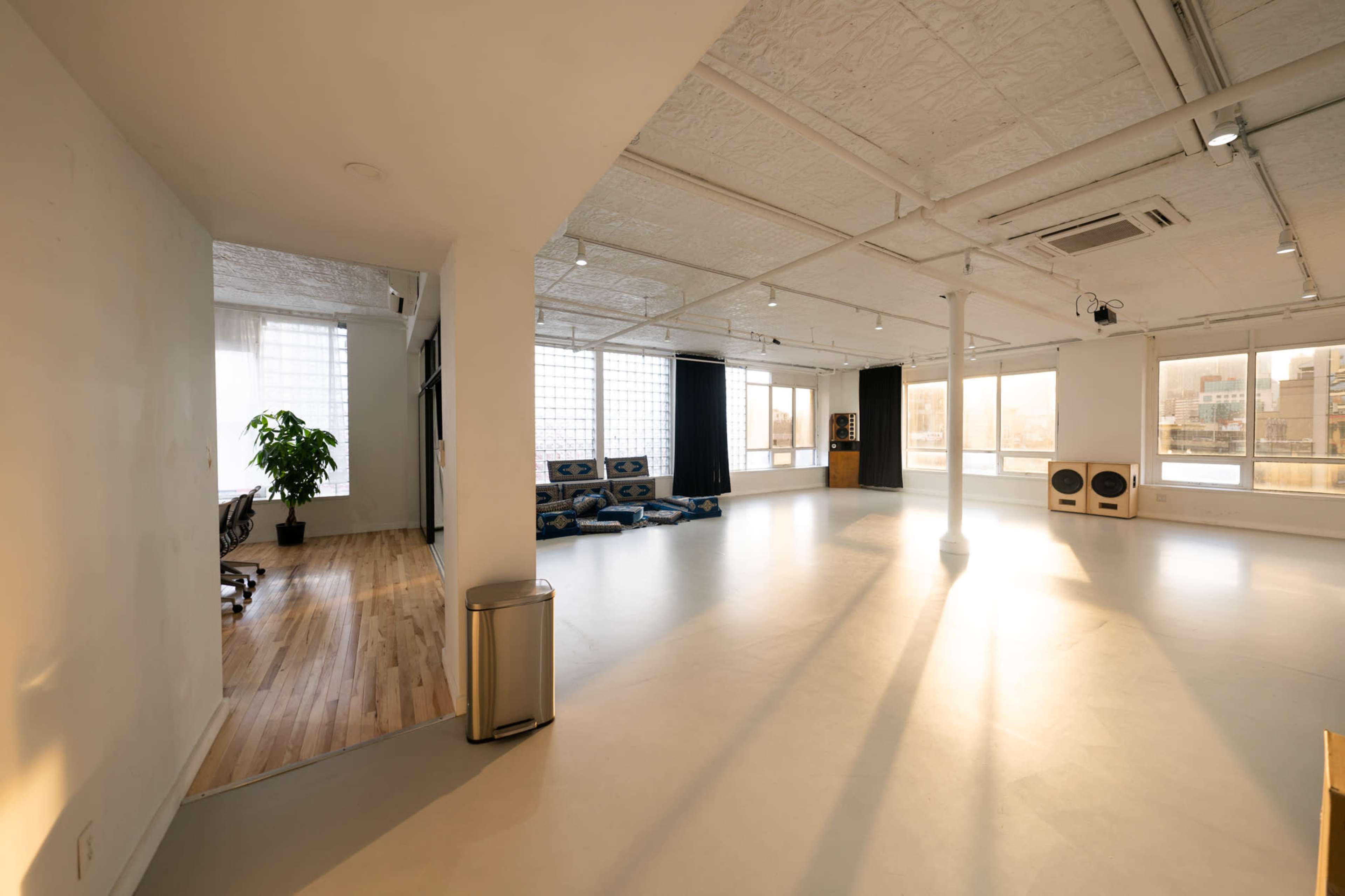 An open-concept workspace with large windows, minimalist decor, and a seating area featuring blue cushions.