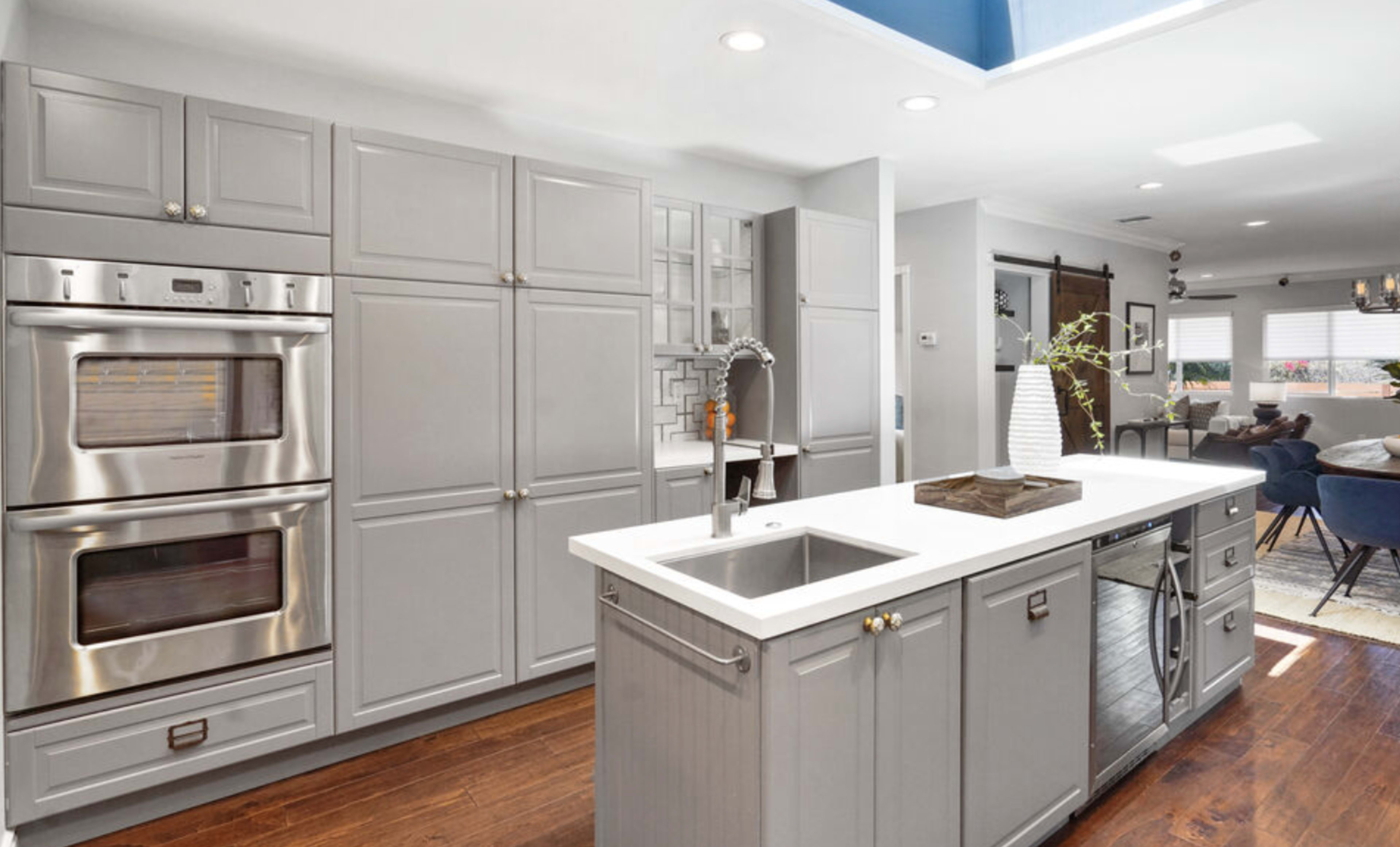 The kitchen features gray cabinetry, stainless steel appliances, and a central island with a sink, complemented by a hardwood floor.
